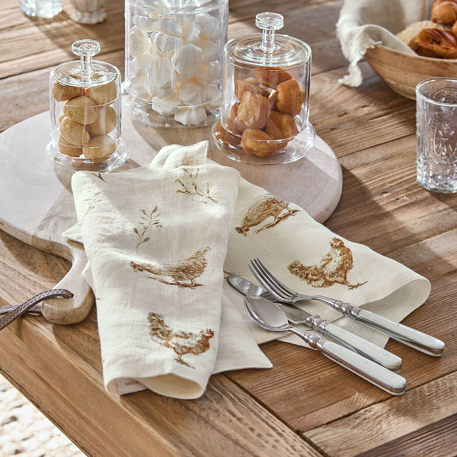 Placemat set van 2 Chavéreau Crèmekleurige linnen servetten met bruine kippenprint op houten tafel met zilverkleurig bestek