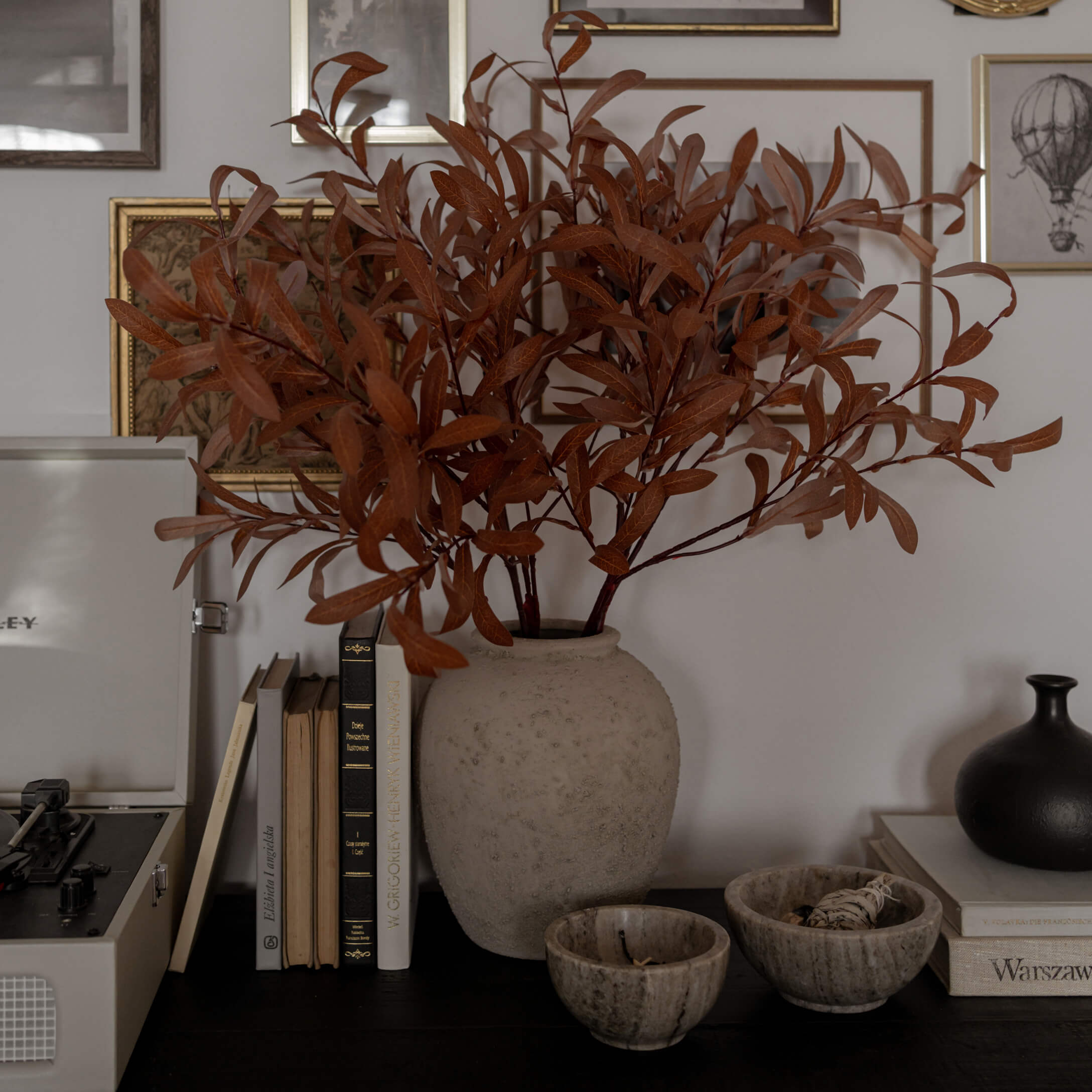 Beige albasten vaas met gedroogde bruine takken op een donkere tafel met boeken en decoratie