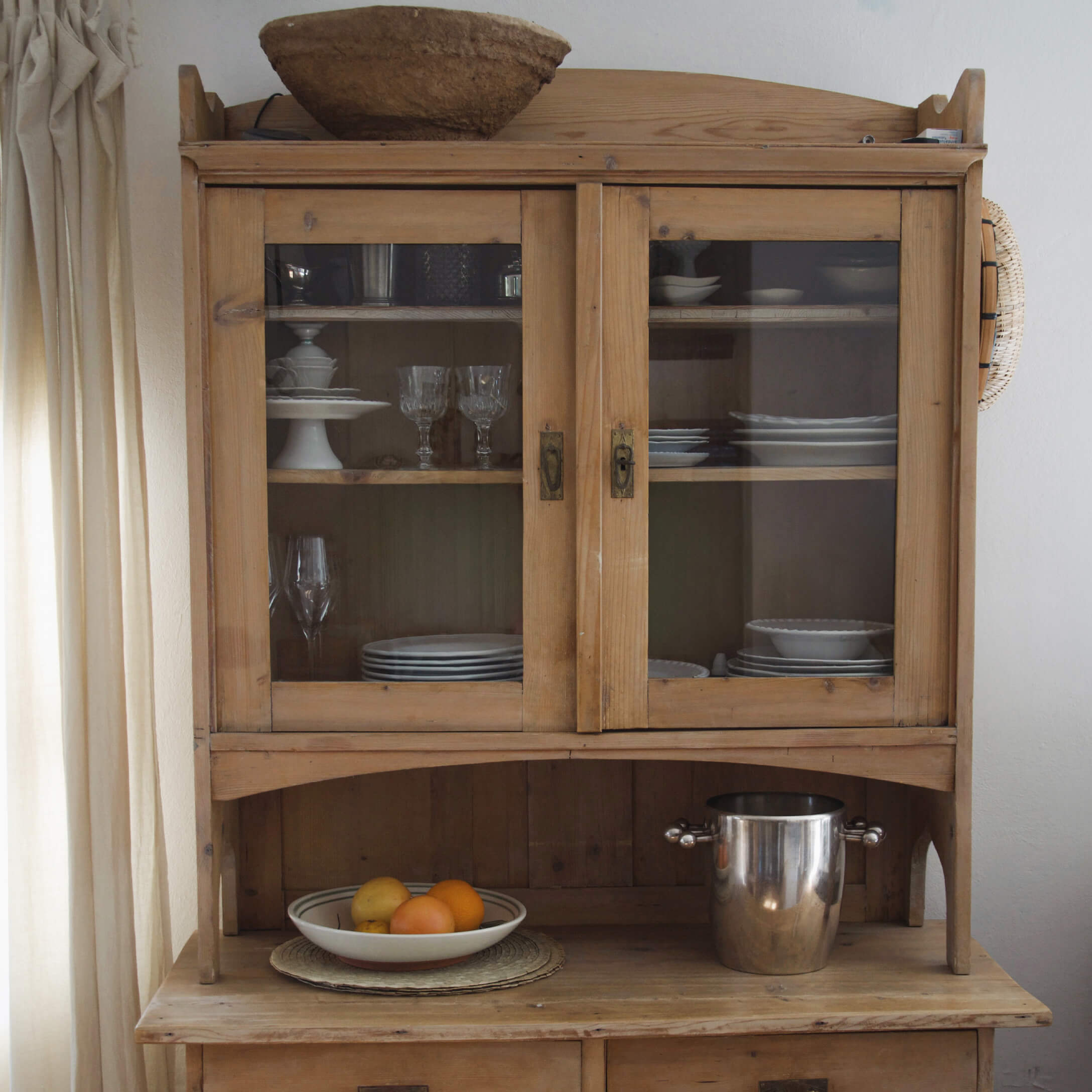 Houten keukenkast met glazen deuren, wit servies en metalen emmer op het blad