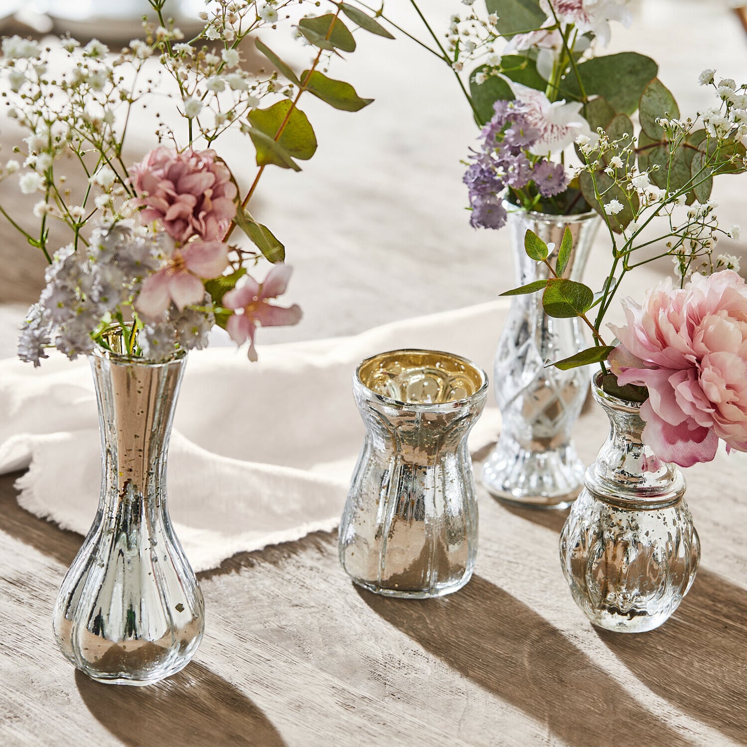 Set van vier zilverkleurige glazen vazen met bloemen op houten tafel, sfeervolle tafeldecoratie