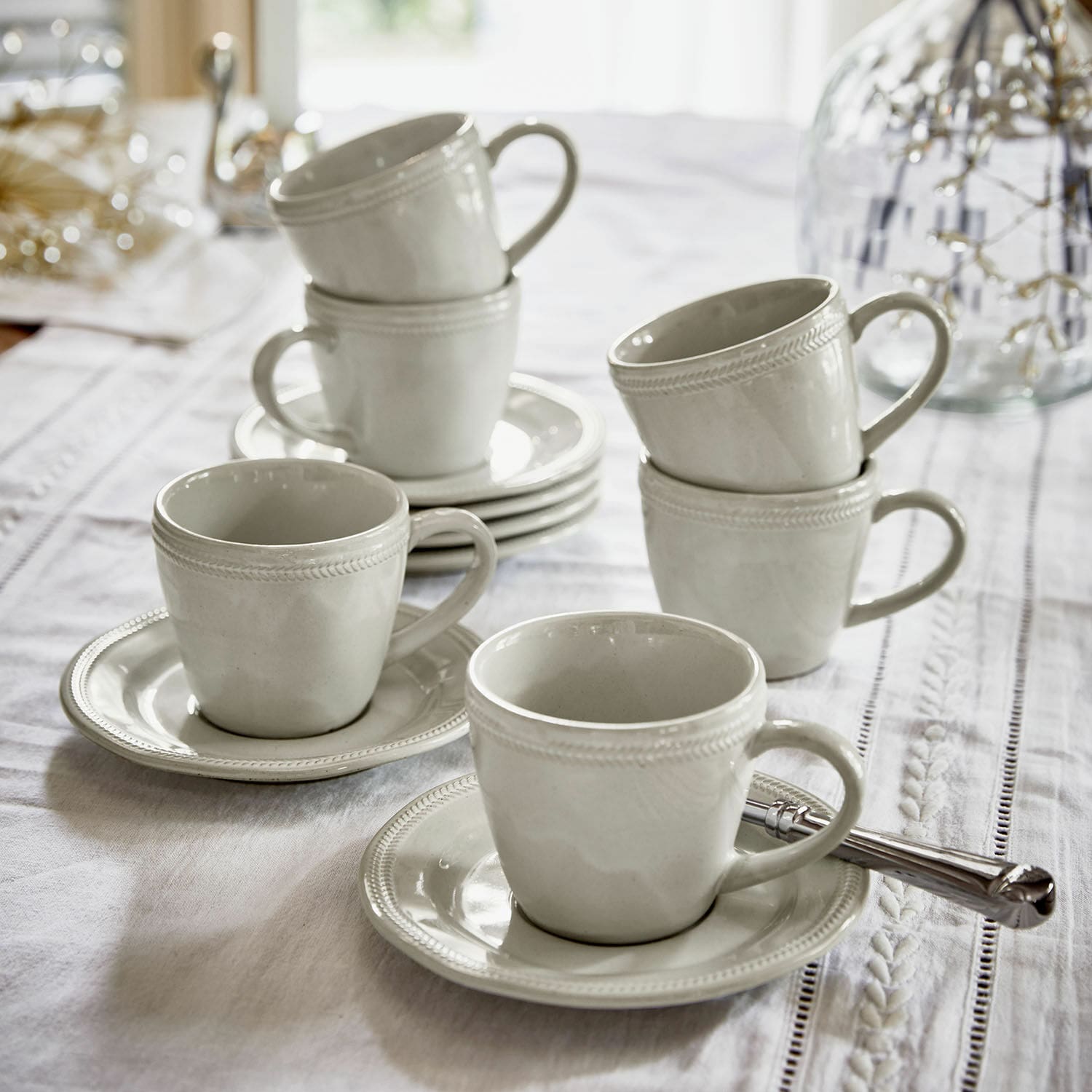 Set witte keramische kopjes met schotels op een wit tafelkleed voor koffie en thee