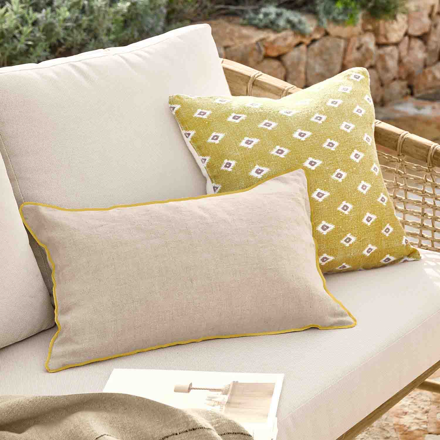 Beige sierkussen met gele bies en geel kussen met wit patroon op rotan bank
