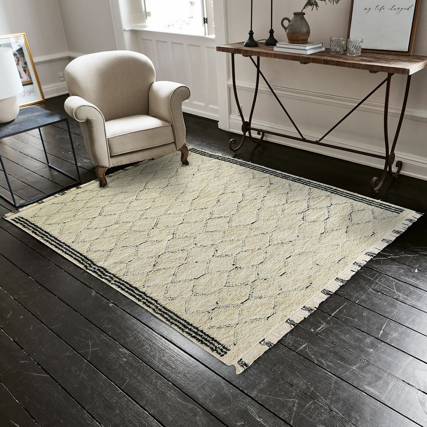 Beige vloerkleed met geometrisch patroon en franjes op donkere houten vloer in woonkamer