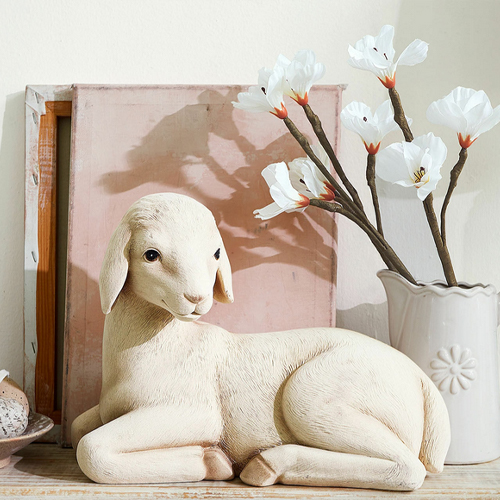 Decoratief lichtkleurig lammetjesbeeld naast vaas met witte bloemen, interieurdecoratie