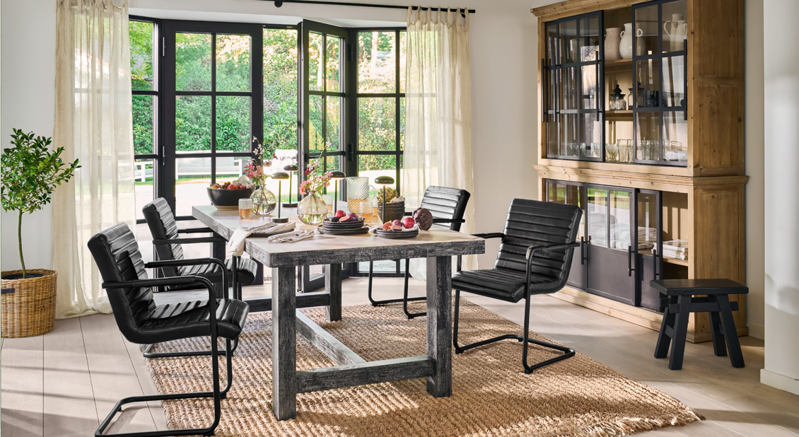 Eetkamer met zwarte leren stoelen en houten tafel op natuurlijke vloerkleed, moderne uitstraling