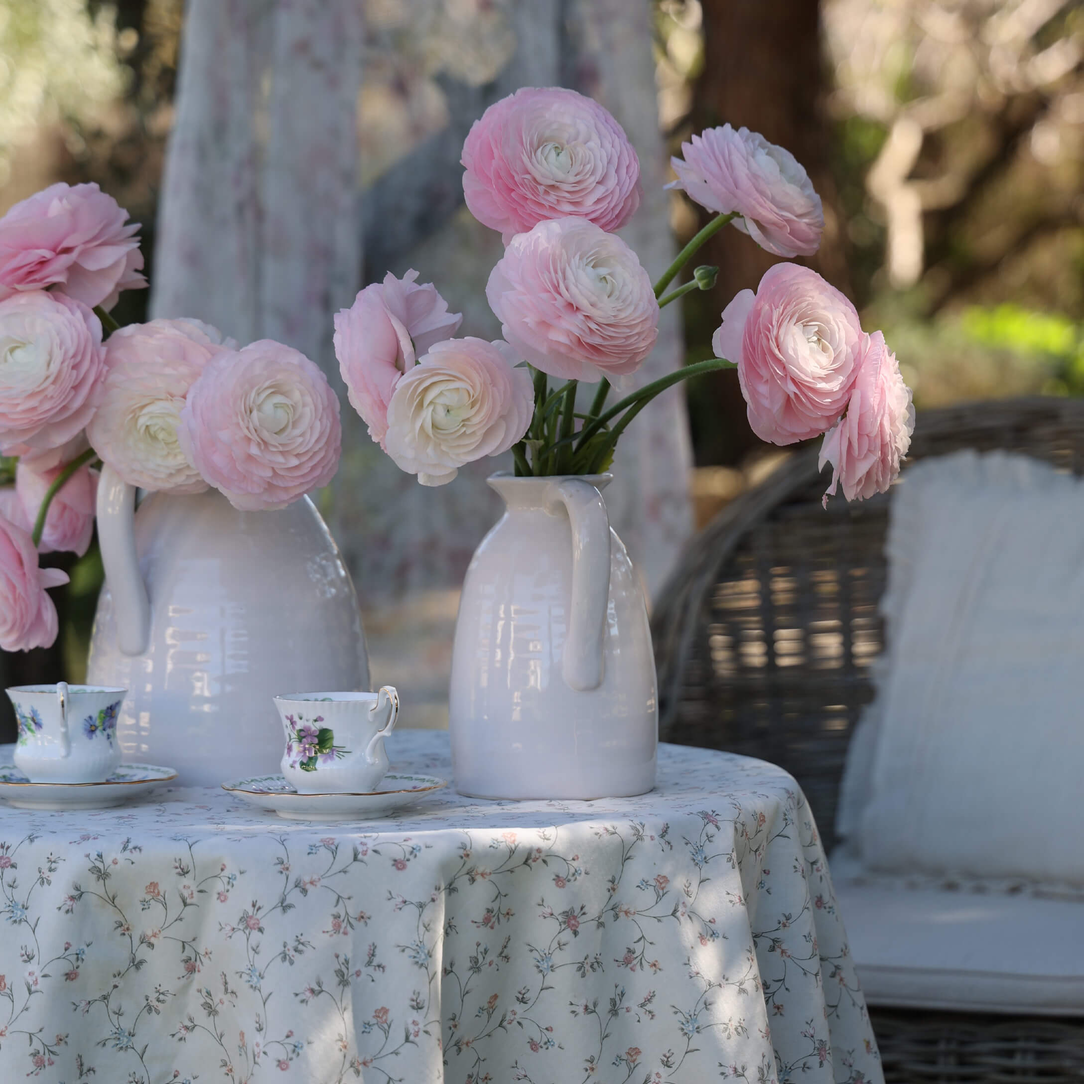 Witte keramische kannen met roze bloemen op een tafel met bloemen tafelkleed en decoratieve theekopjes