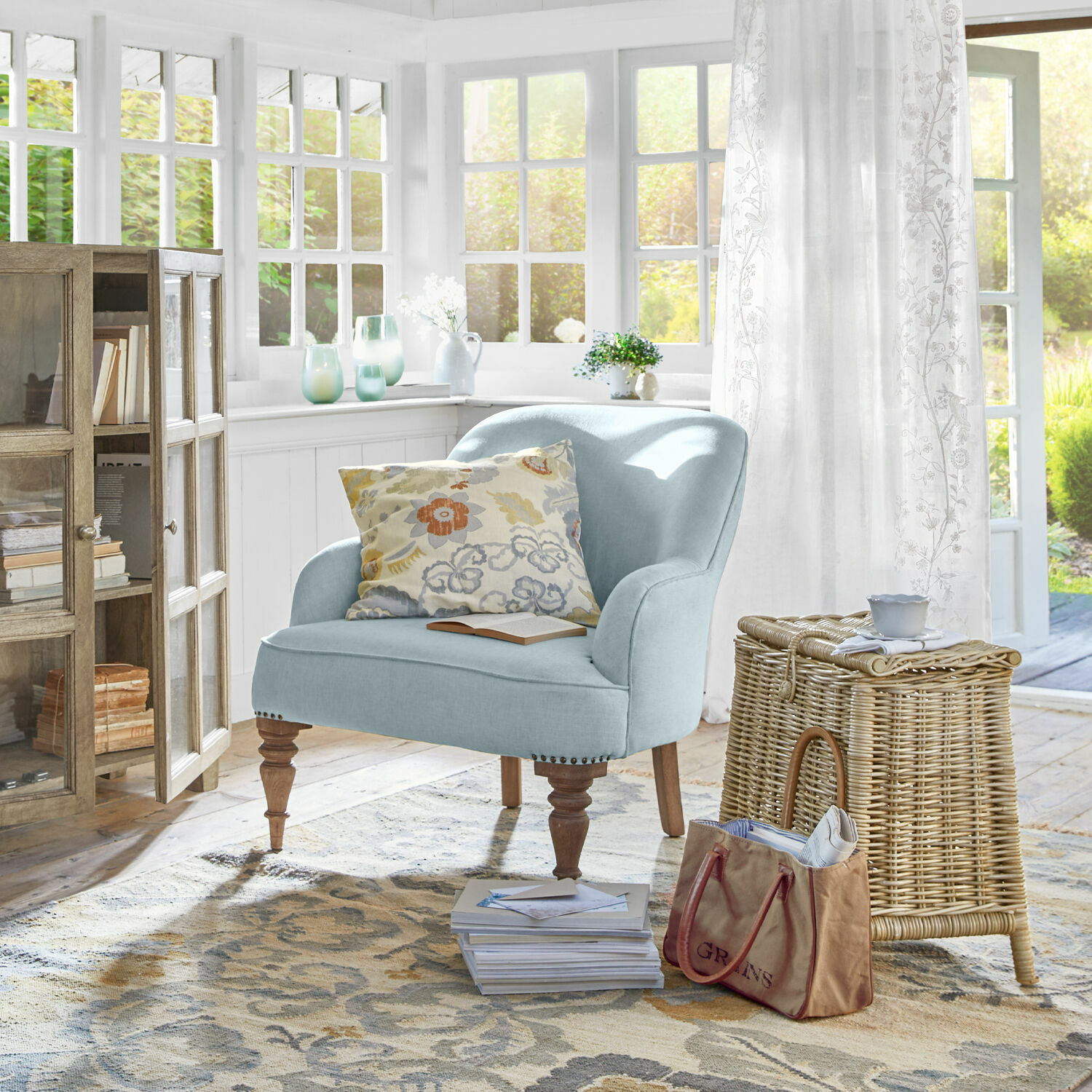 Lichtblauwe gestoffeerde stoel met houten poten in lichte woonkamer met rieten mand en bloemkussen
