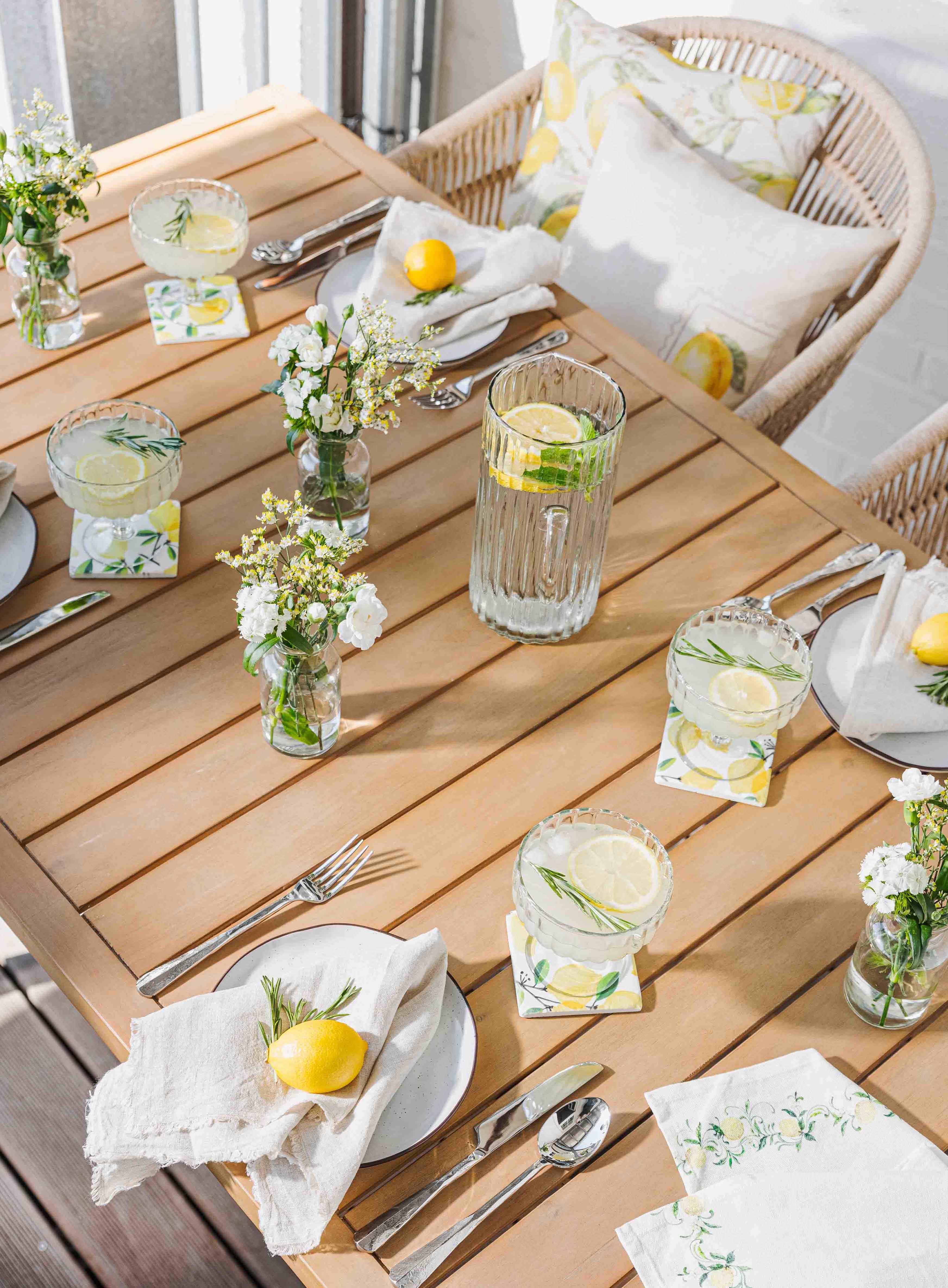 Lichte houten tafel met limonade, glazen en citroendecoratie voor zomerse tuintafel sfeer