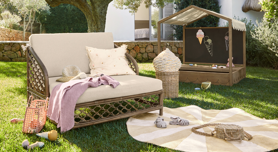 Tuin met beige rotan bank en houten speelhuisje voor kinderen op groen gras