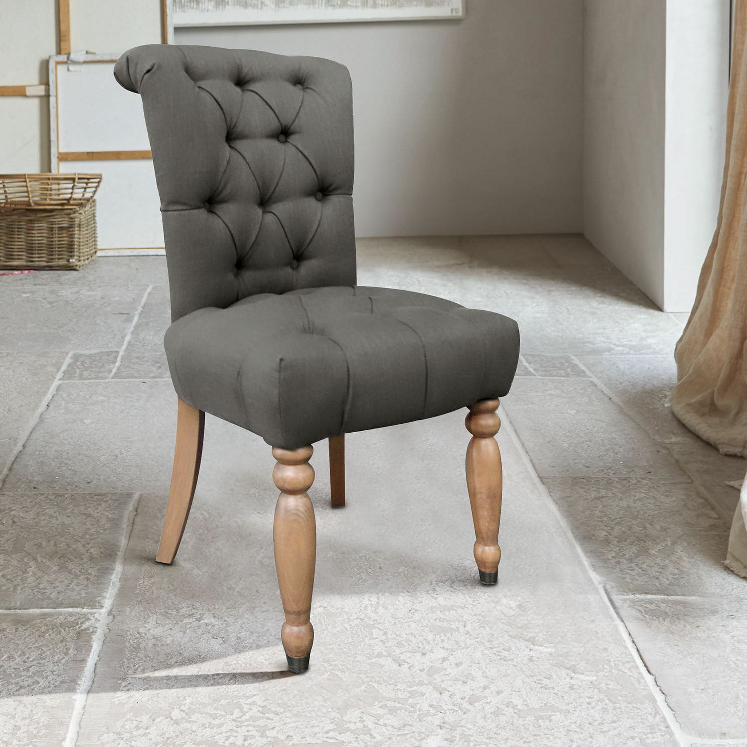 Grijze gestoffeerde stoel met houten poten op stenen vloer in lichte kamer