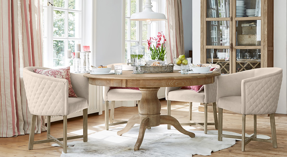 Eetkamer met ronde houten tafel en beige gestoffeerde stoelen in landelijke stijl met decoratie