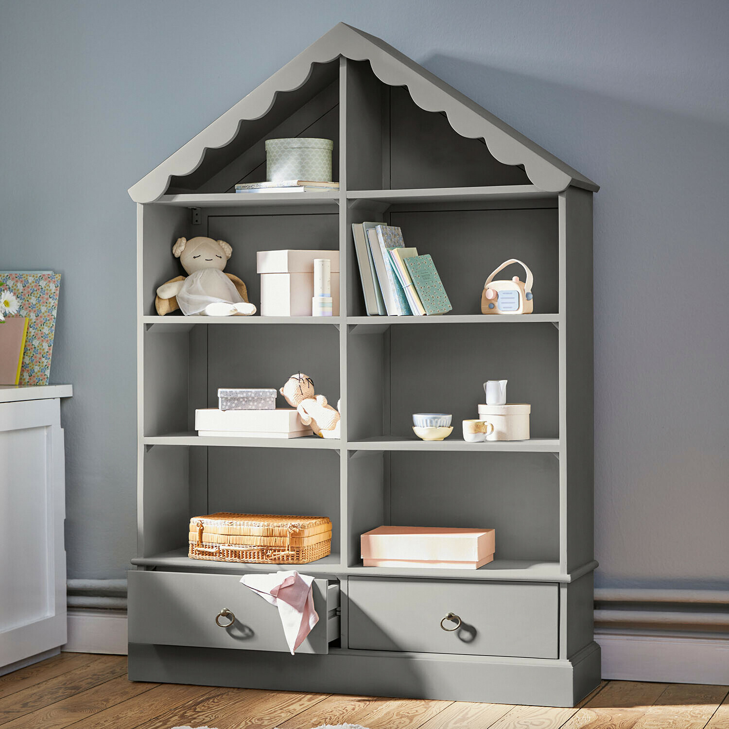 Grijze houten kast in huisvorm met speelgoed en boeken voor kinderkamer
