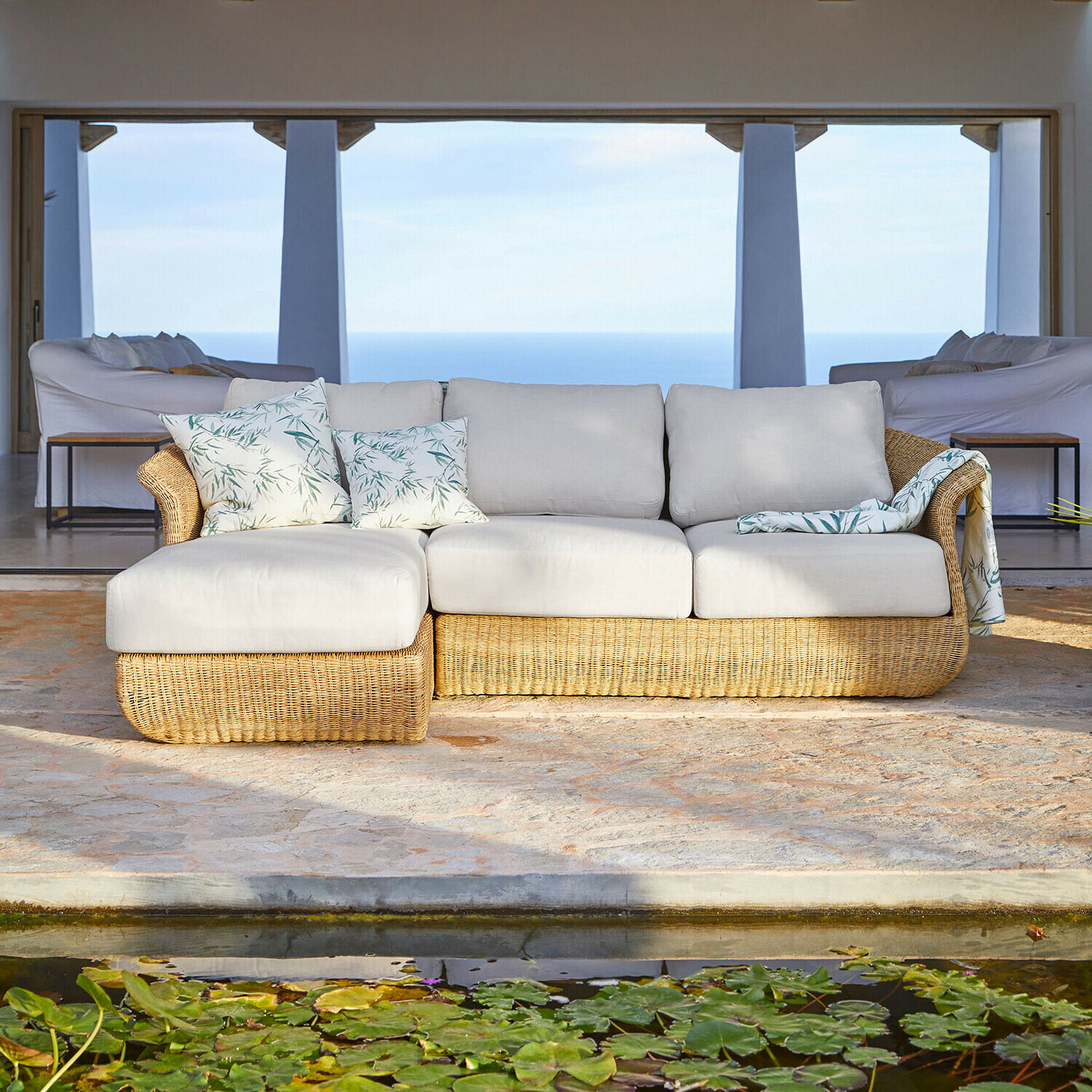 Rotan bank met lichtgrijze kussens en decoratieve kussens met bladmotief, tuinmeubilair