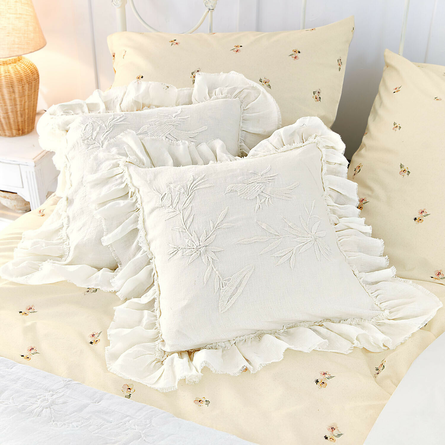 Beige beddengoed met klein bloemenpatroon en crèmekleurige linnen kussens met ruches en vogelborduursel