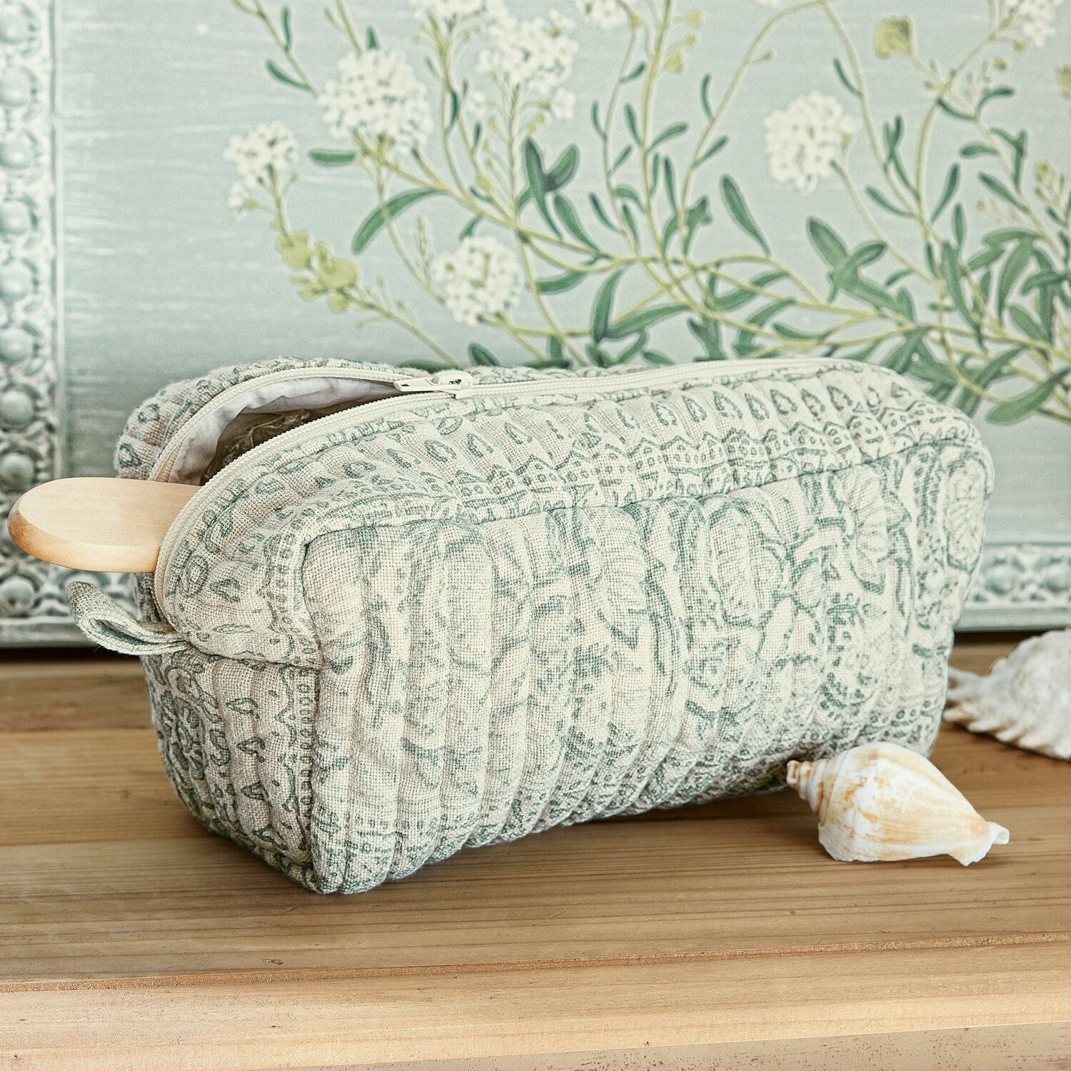 Gewatteerde make-uptas van stof met groen-beige patroon op houten tafel met schelp