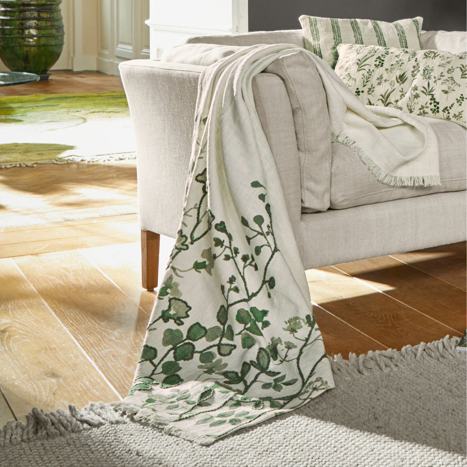 Beige deken met groen plantenpatroon op bank, zacht materiaal, sfeervolle woondecoratie