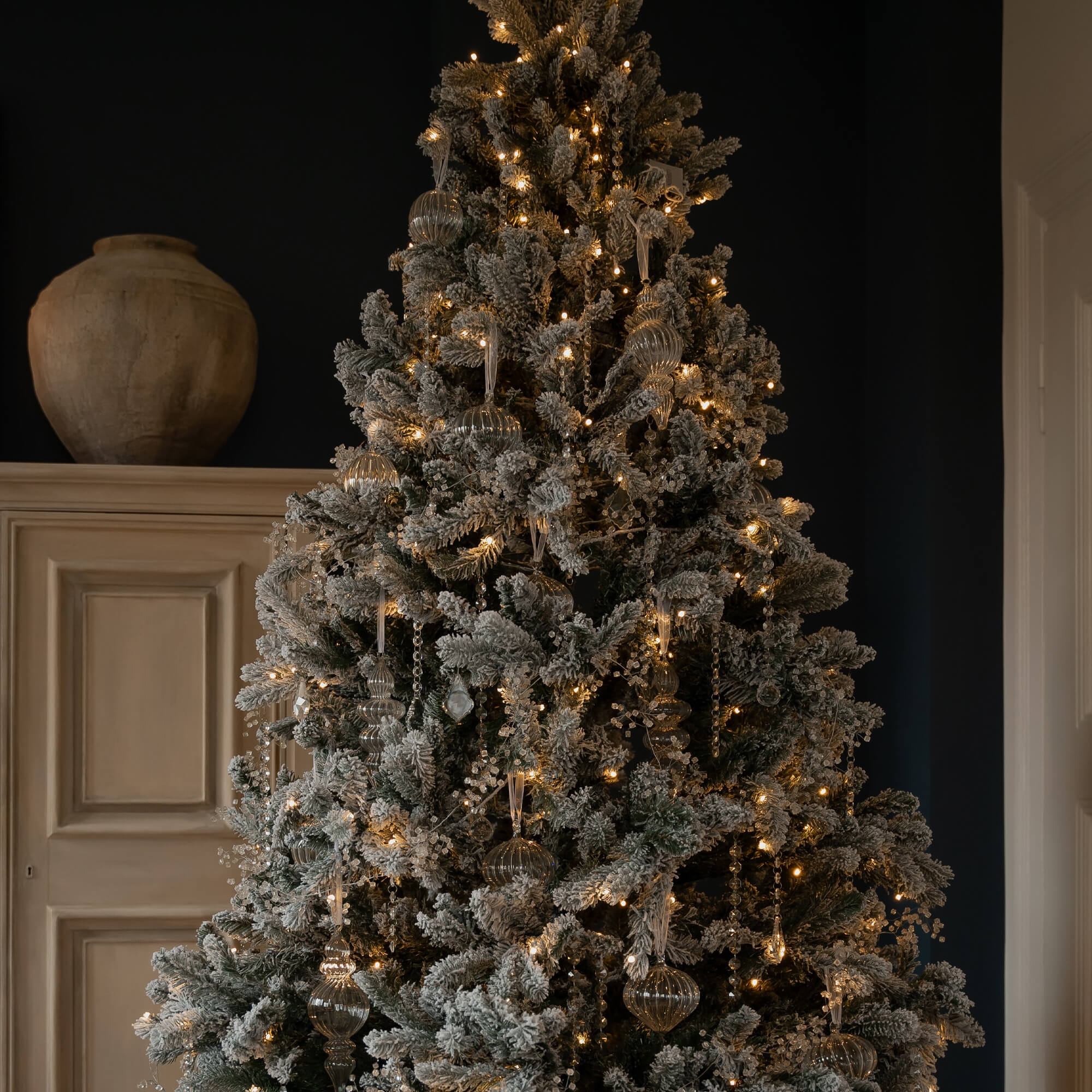 Kunstmatige besneeuwde kerstboom met warme verlichting en transparante versieringen voor feestdagen