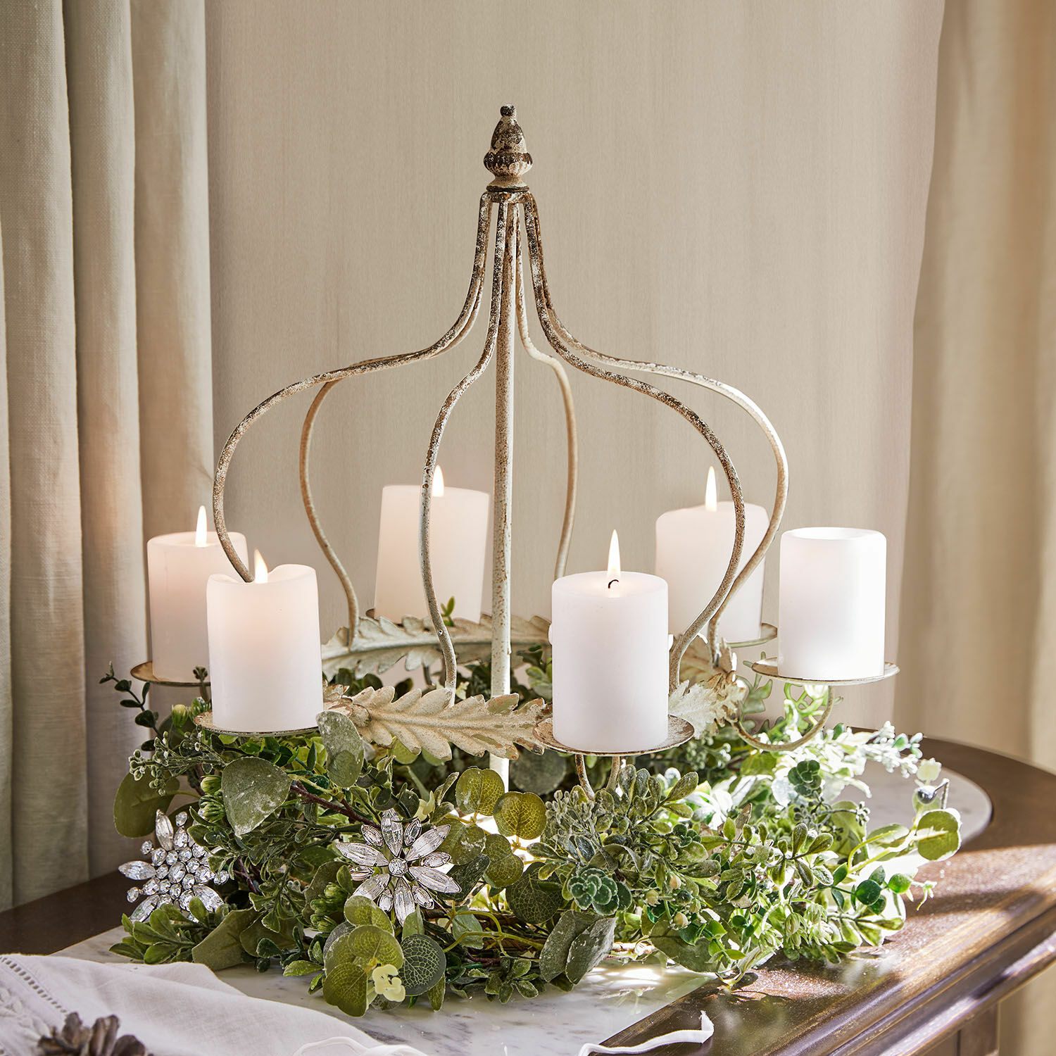 Metalen kandelaar in kroonvorm met witte kaarsen en groene decoratie op tafel