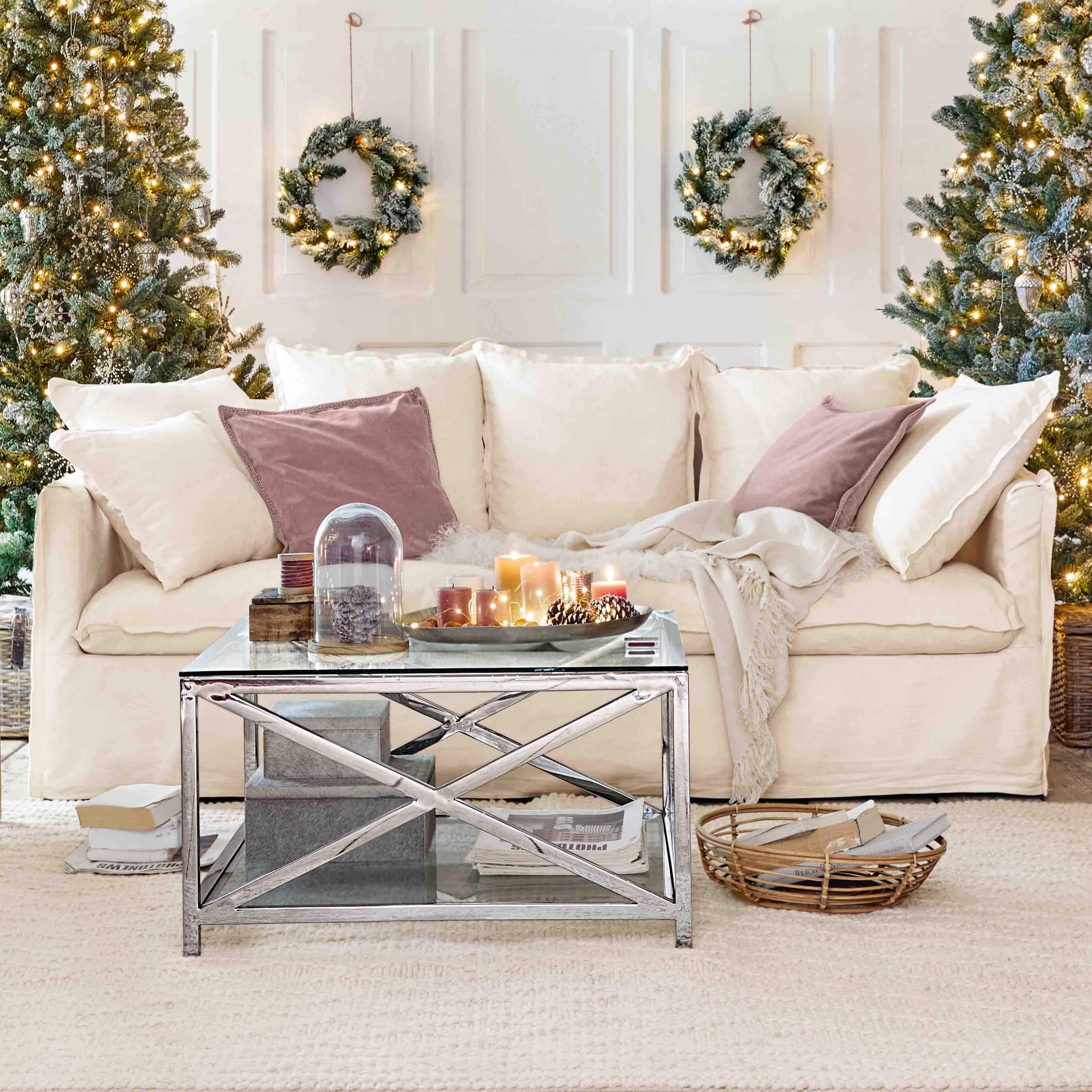 Comfortabele crèmekleurige bank met kussens en metalen salontafel in kerstdecor met bomen en kransen