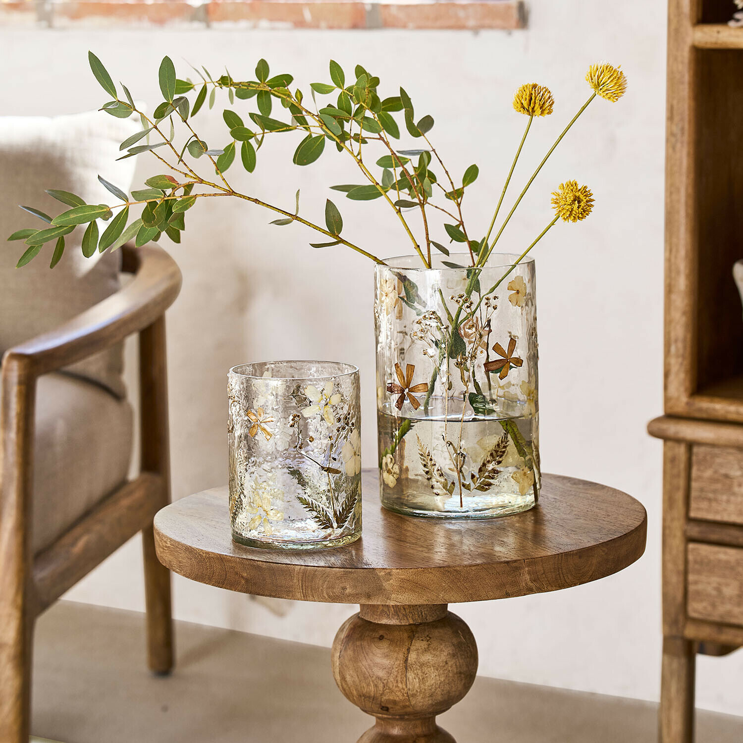 Glazen vazen met gedroogde bloemen en bladeren op houten tafel in lichte kamer