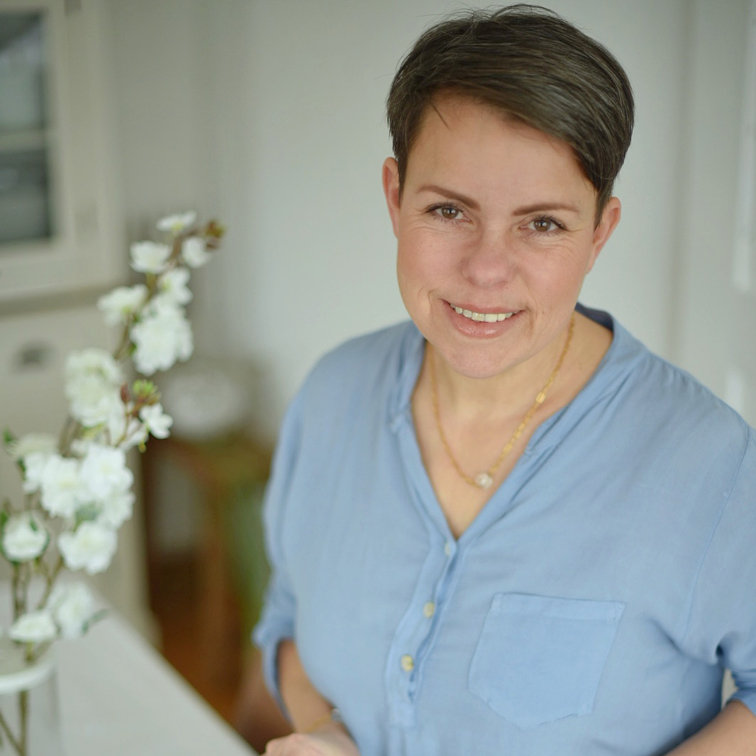 Lachende vrouw in blauw overhemd naast witte bloemen in lichte kamer