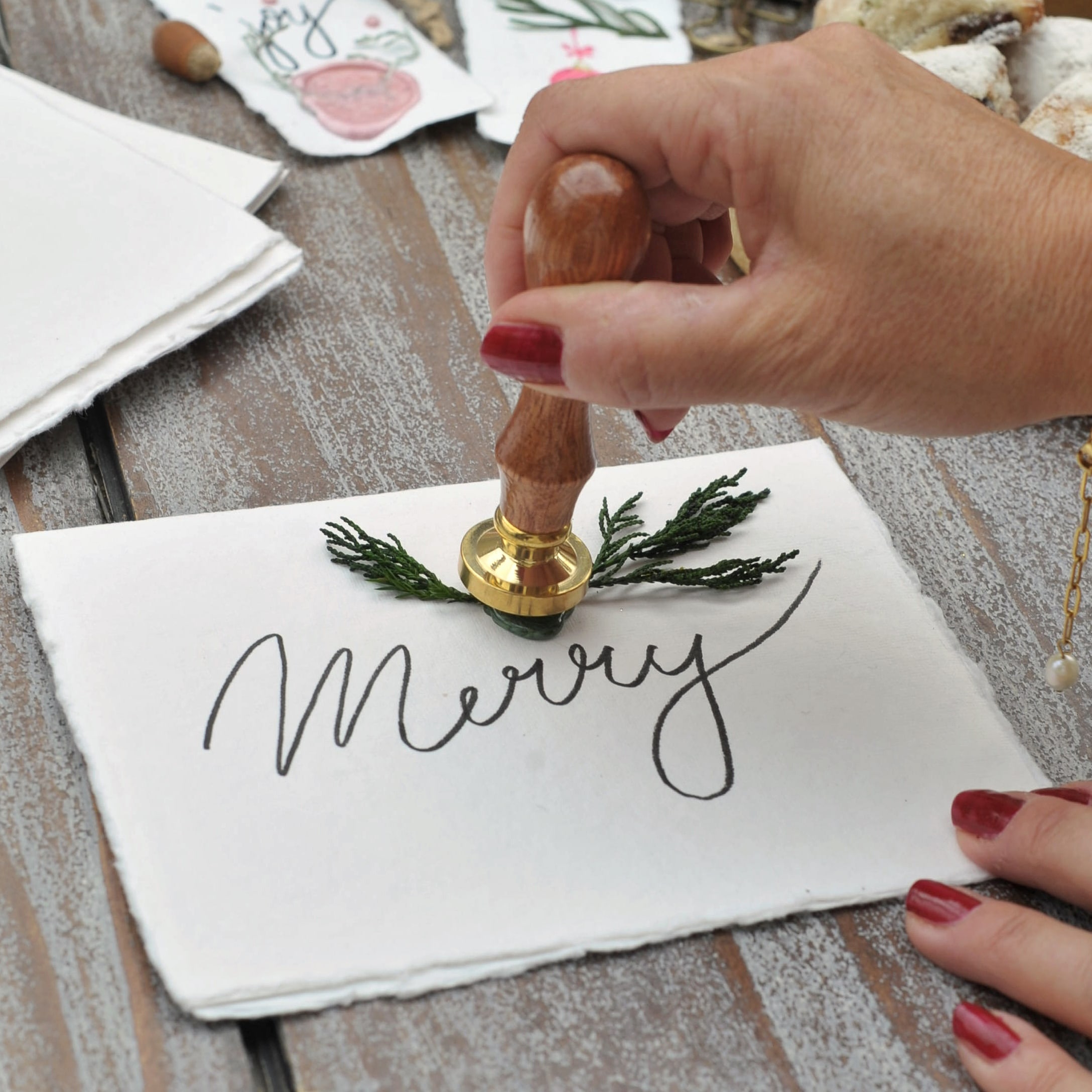Hand met rode nagellak gebruikt houten zegel om witte kaart met tekst Merry te versieren