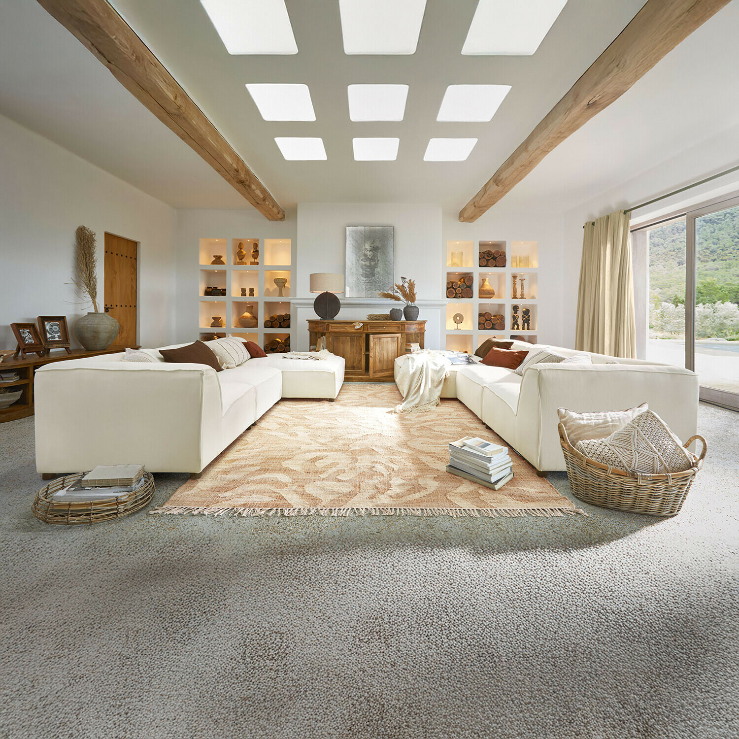 Ruime woonkamer met witte bank, houten balken, natuurlijke decoraties, beige vloerkleed en groot raam