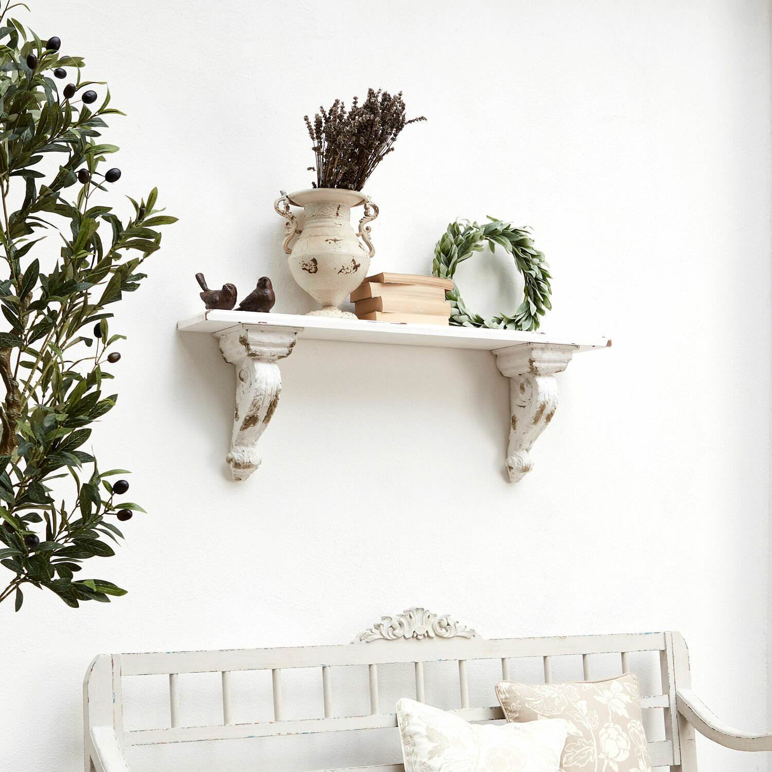 Witte houten wandplank met decoratieve beugel, vaas, boeken en groene krans