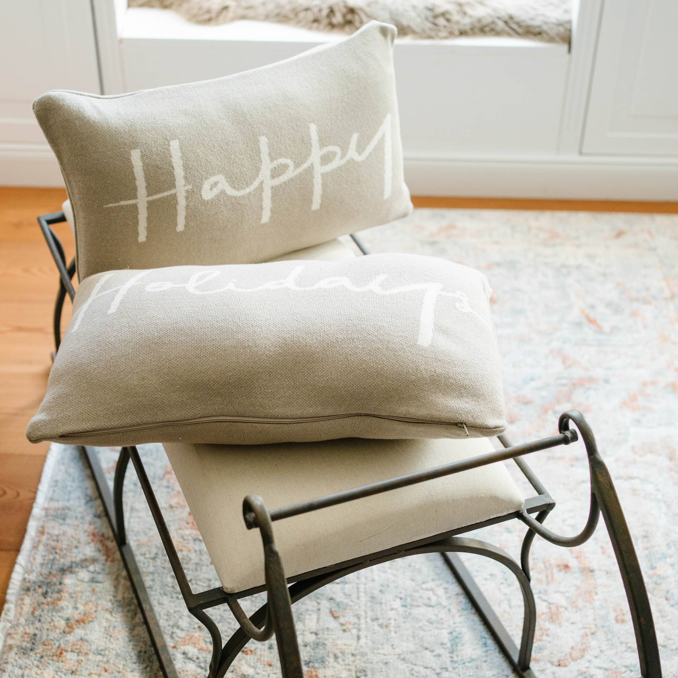 Beige sierkussens met tekst Happy Holidays op metalen frame op lichte vloerkleed