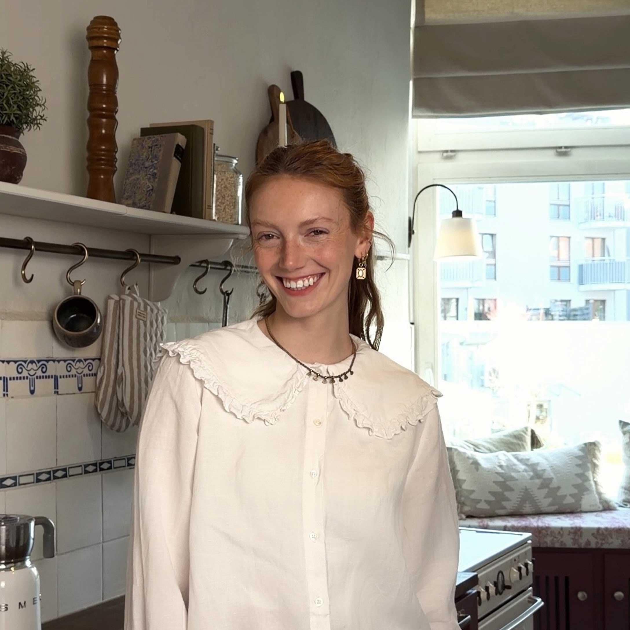 Vrouw in witte blouse met ruches in lichte keuken met decoratieve accessoires en raam