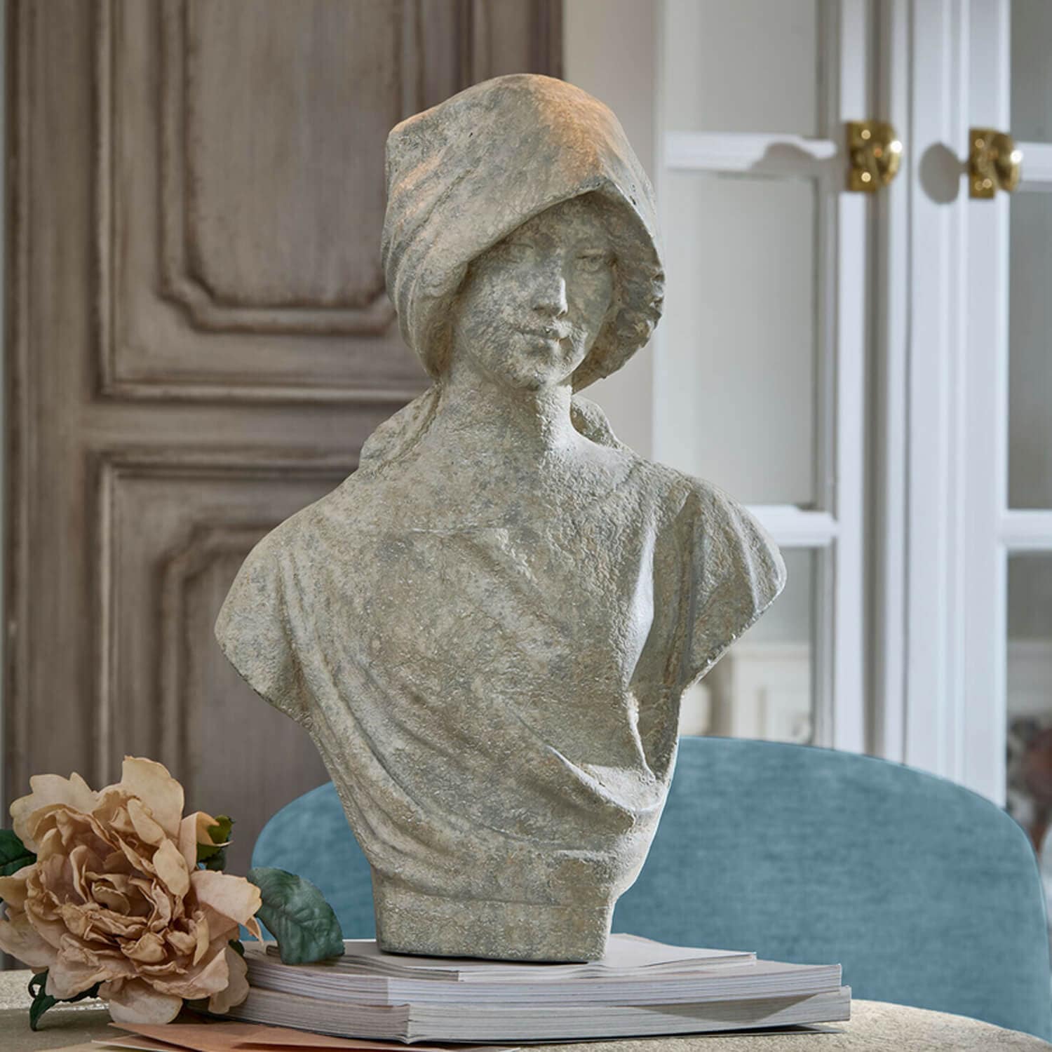 Grijs stenen vrouwenbuste op stapel boeken met beige bloem ernaast, interieurdecoratie