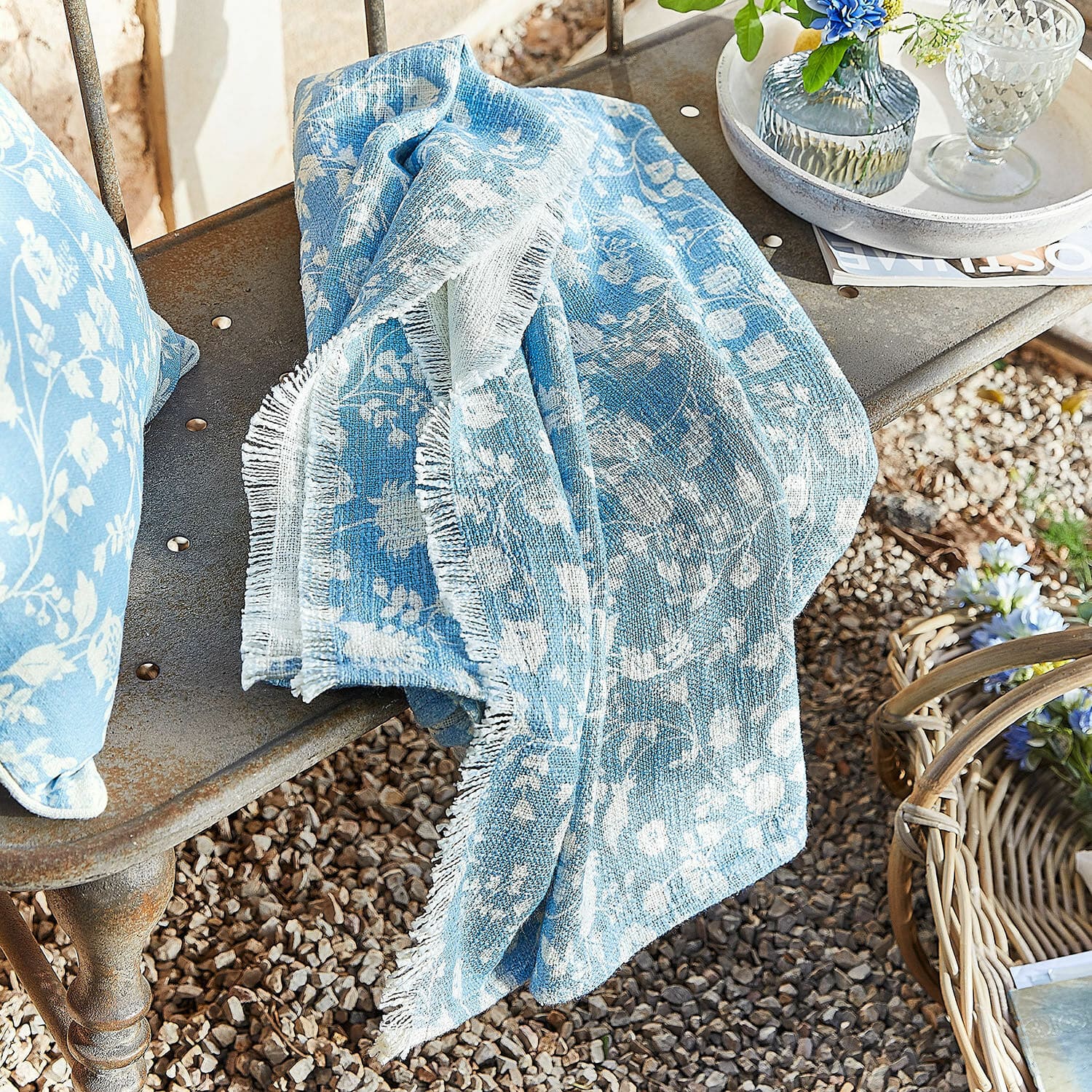 Plaid Corvelique Blauwe katoenen deken met wit bloemenpatroon op metalen bank in de tuin