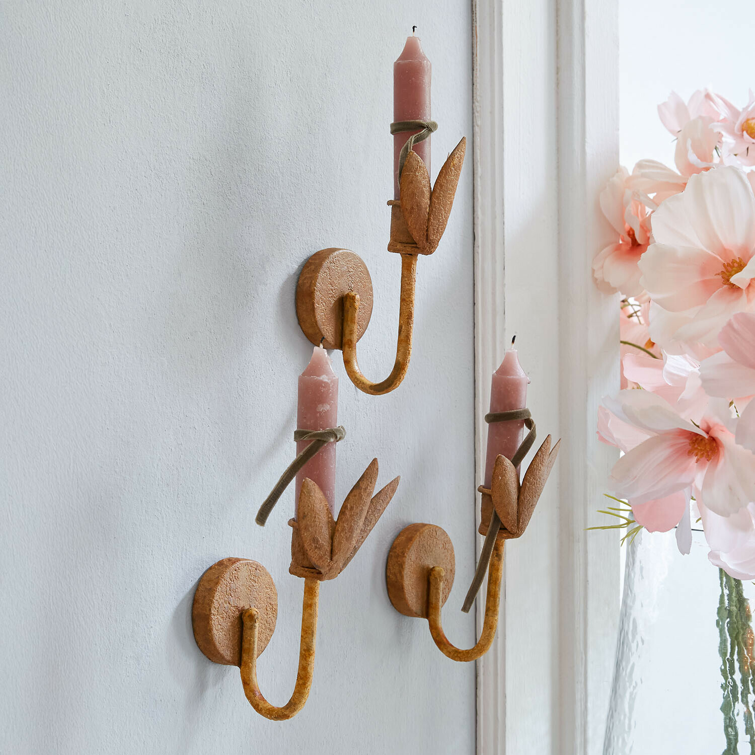 Set van drie metalen wandkandelaars in roestkleur met roze kaarsen en bladdecoratie