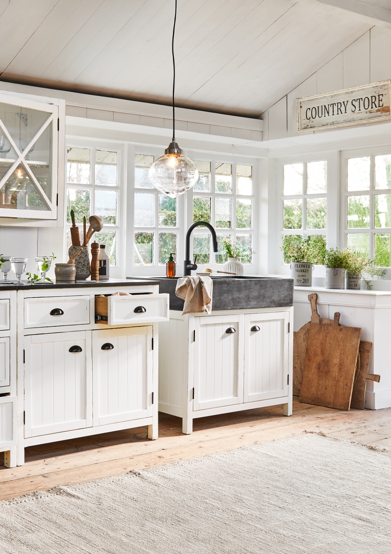 Landelijke keuken met witte houten kasten en zwarte stenen gootsteen, planten als decoratie