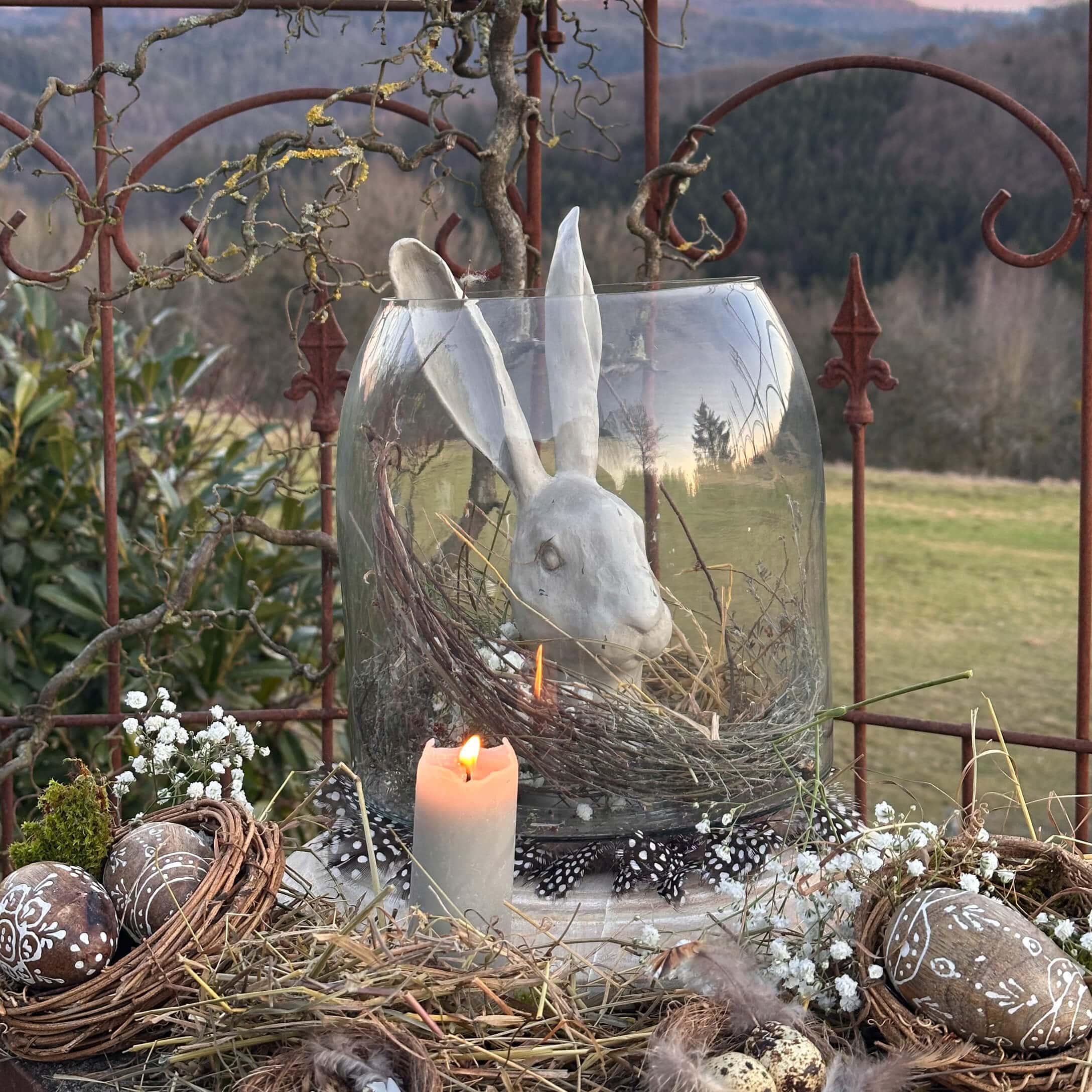 Paasdecoratie met witte keramische haas in glazen pot en brandende kaars rustiek