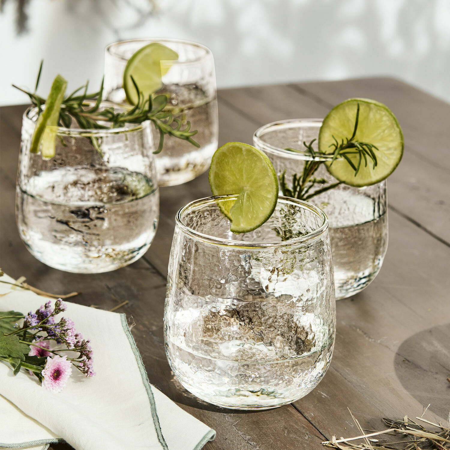 Glas set van 4 Valters Set van vier glazen van hamerslagglas met limoenplakjes en rozemarijn takjes op houten tafel