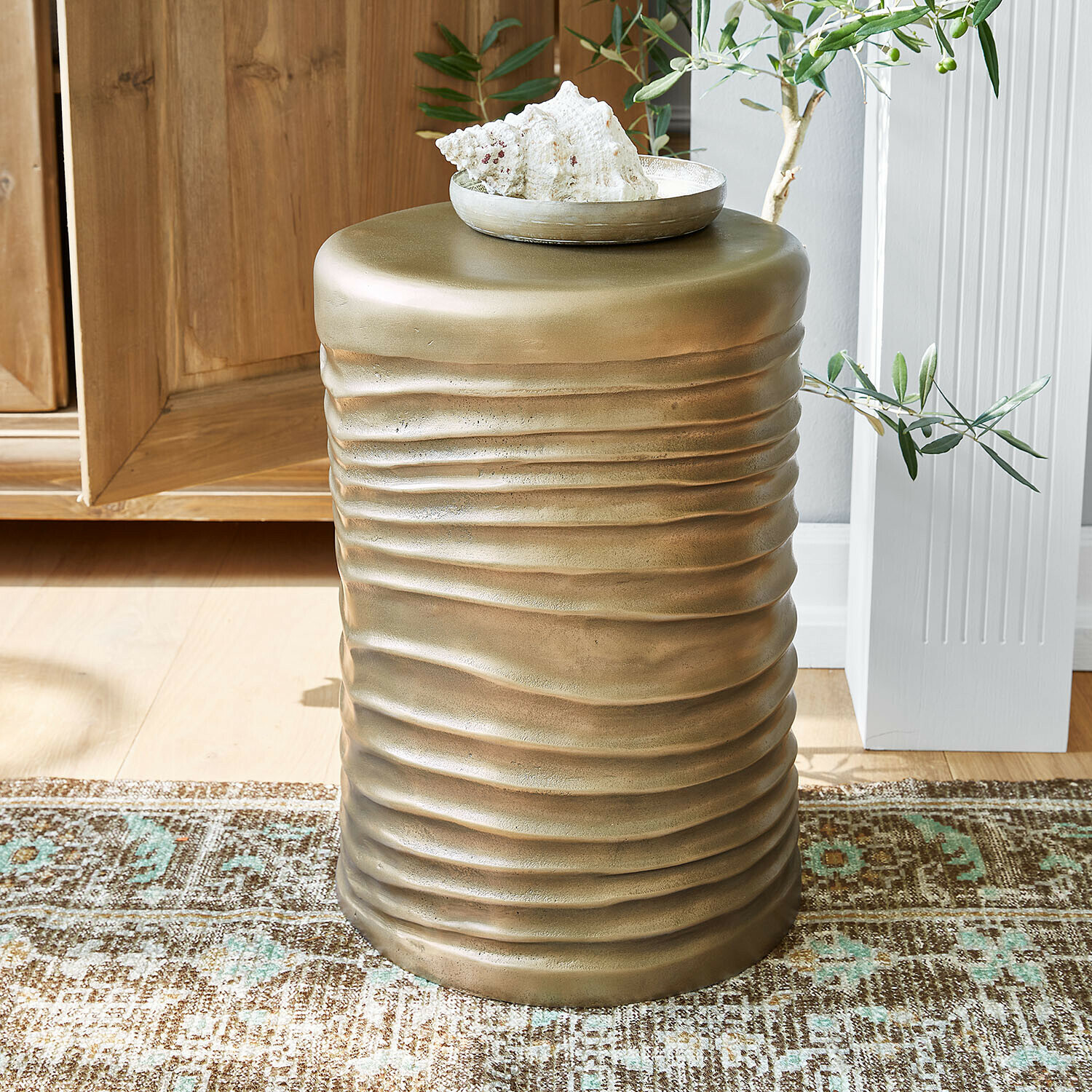 Gouden metalen bijzettafel met golvende textuur op tapijt in lichte kamer