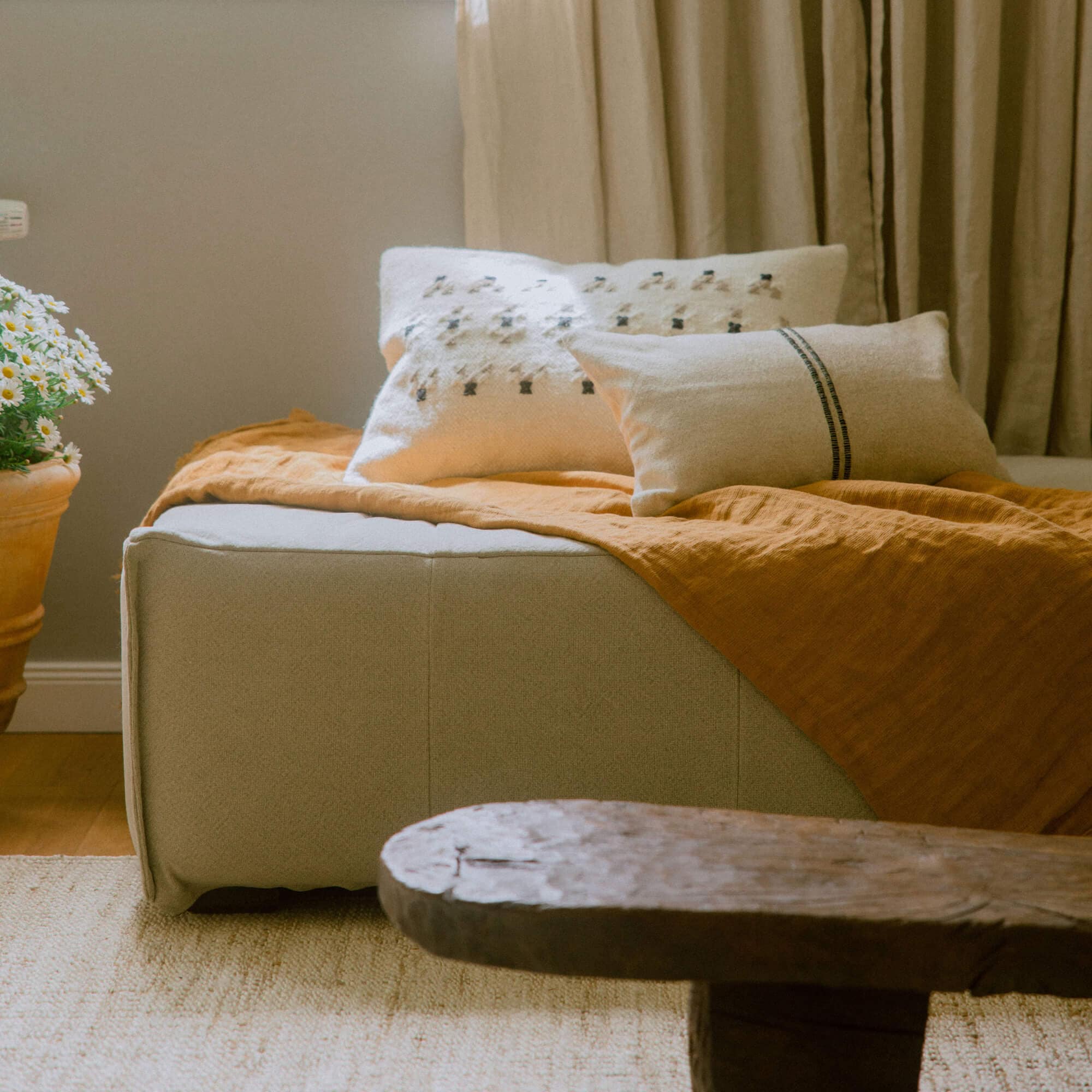 Beige stoffen poef met oranje deken en decoratieve kussens in een gezellige kamer