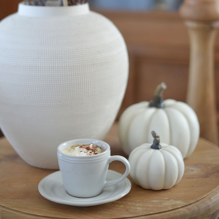 Witte keramische kop met koffie en slagroom op houten tafel naast witte decoratieve pompoenen en vaas