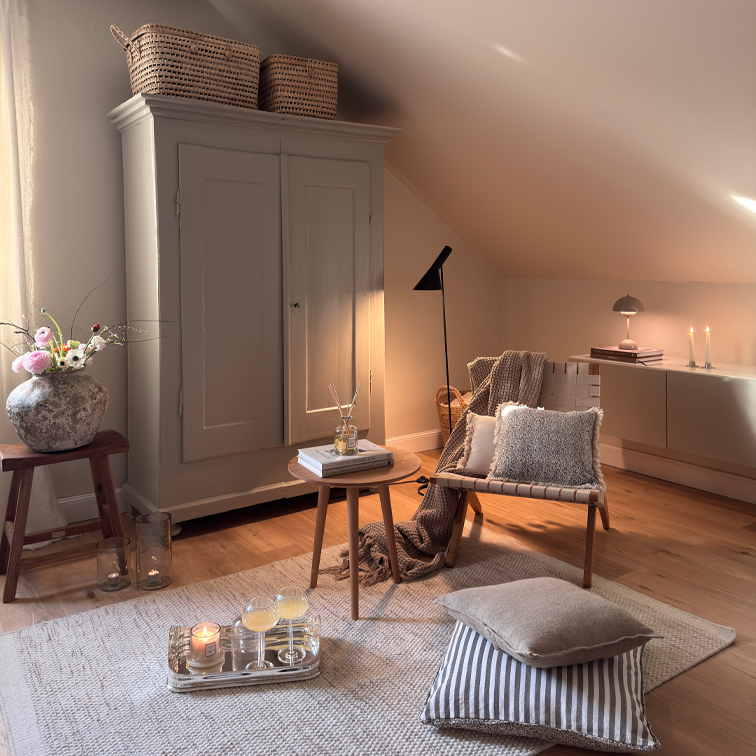 Gezellige woonkamer met beige stoel, houten tafel en kast onder schuine wand, decoraties en lampen