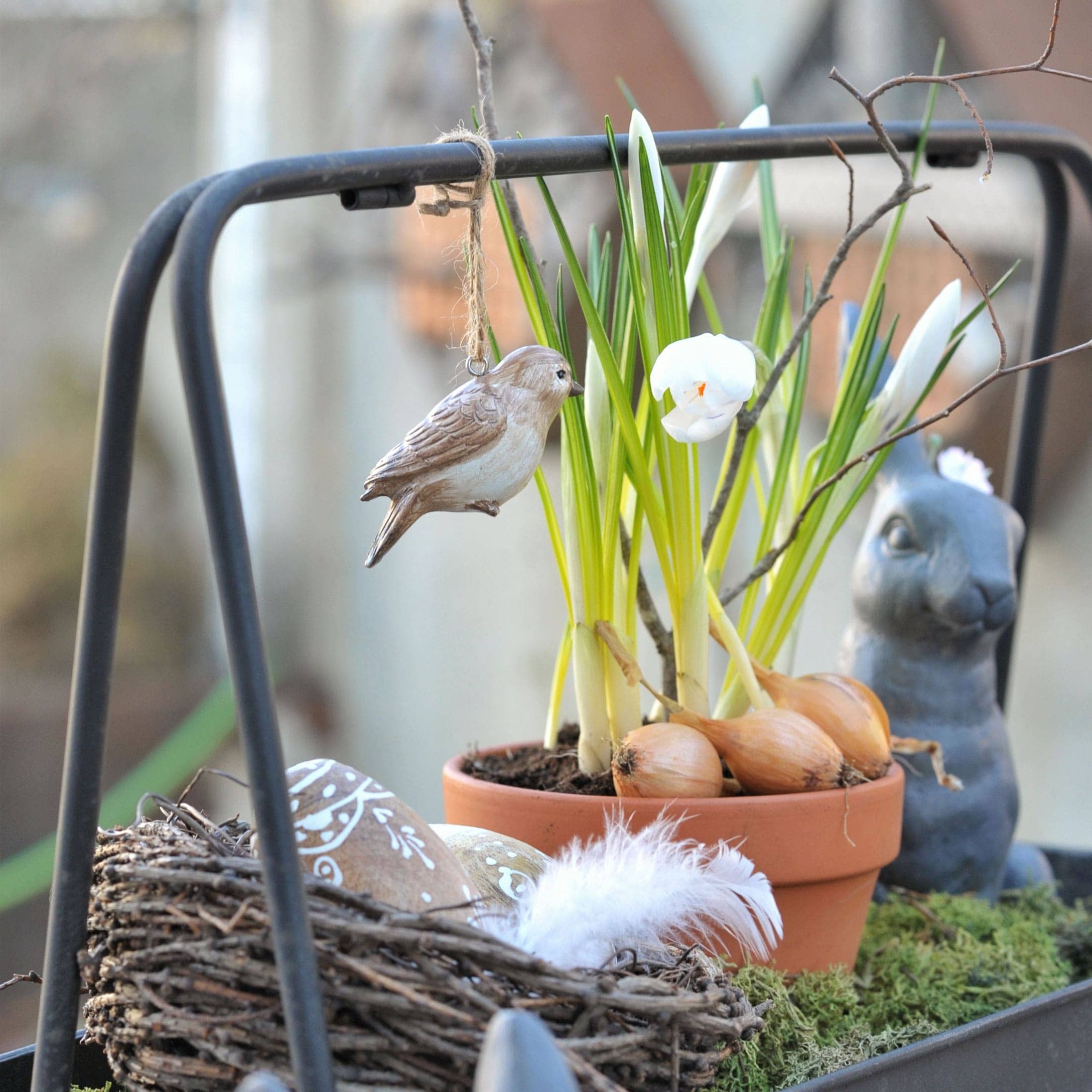 Decoratieve houten vogel hangend bij bloempot met bollen en witte bloemen voor lentebloemstuk