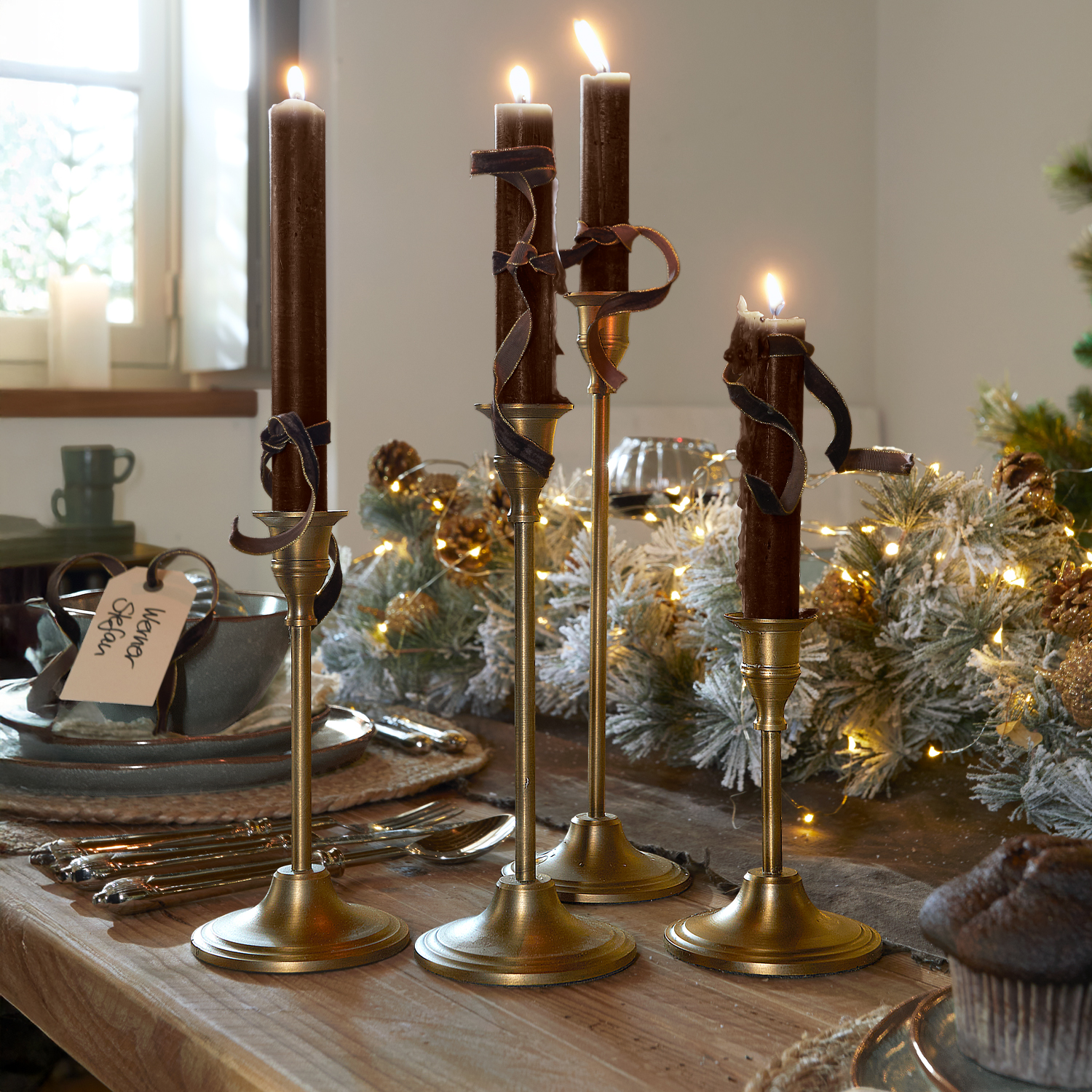 Set van vier gouden kandelaars met bruine kaarsen en decoratieve linten op een houten tafel
