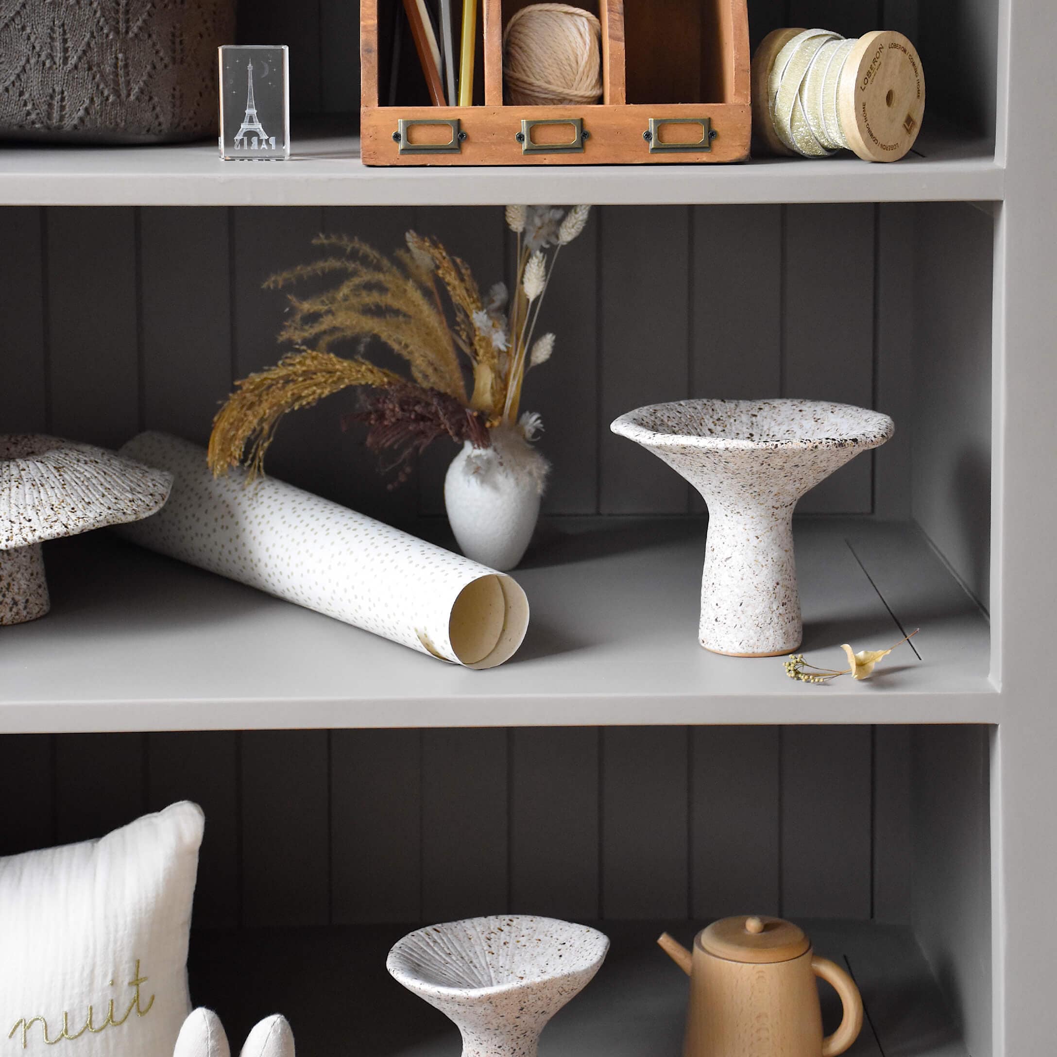 Witte keramische schaal met bruine vlekken op grijze plank met decoraties en gedroogde bloemen
