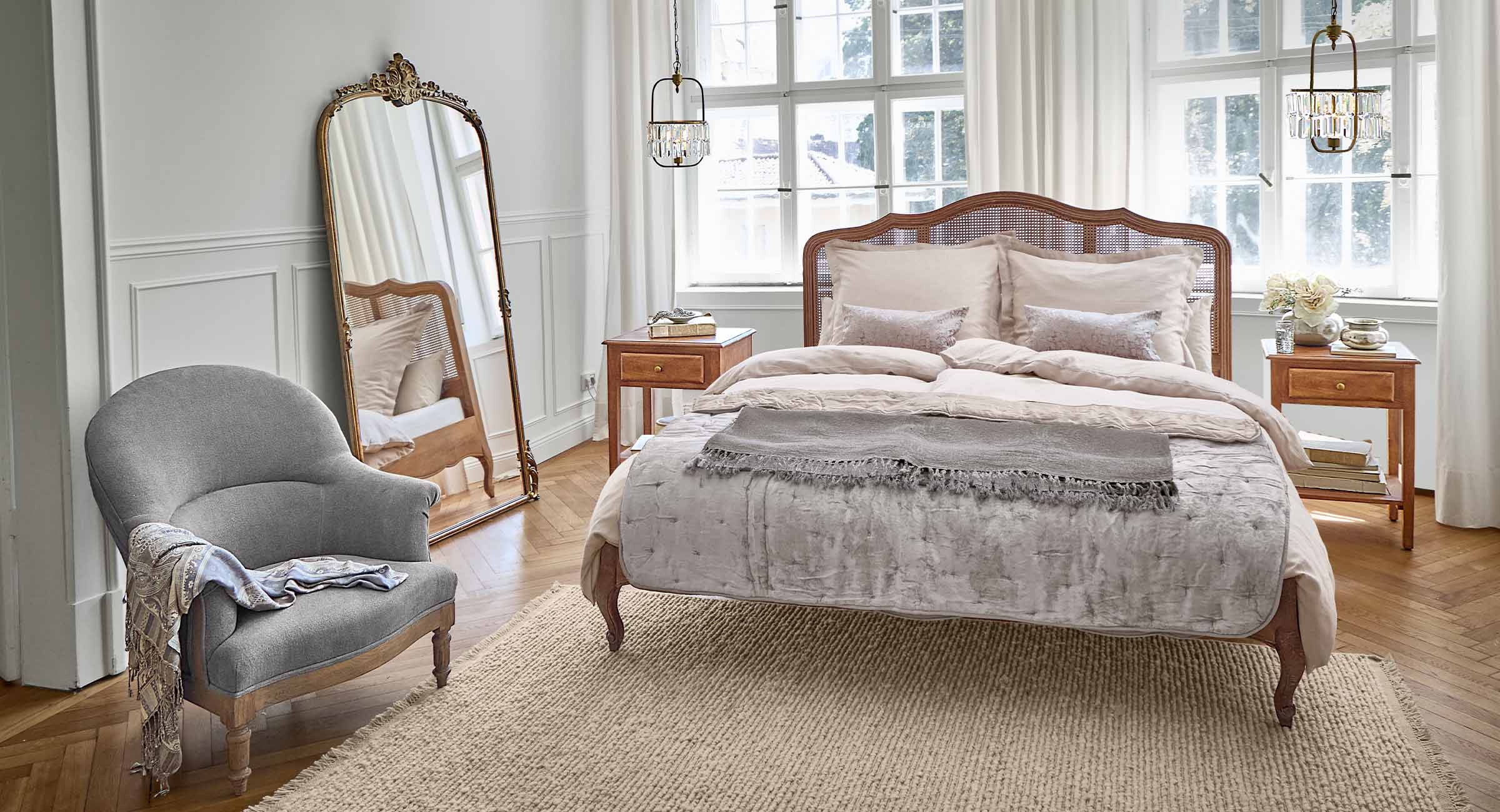 Slaapkamer met bed van rotan en mangohout in beige tinten, grijze fauteuil en natuurlijke vloerkleed