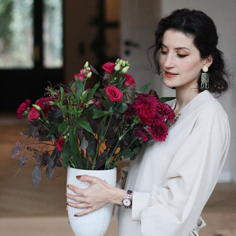 Vrouw in lichte blouse houdt witte keramische vaas met rode bloemen binnen vast