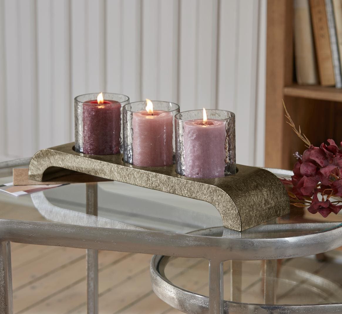 Drie brandende kaarsen in glazen op een gouden metalen standaard op een glazen tafel