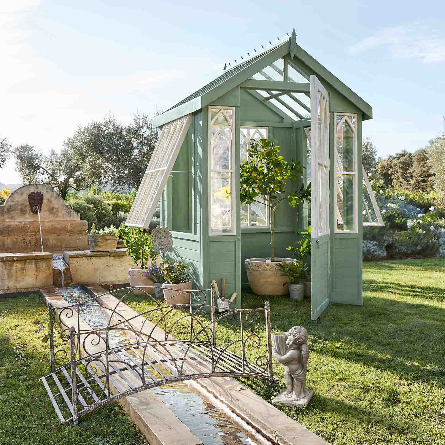Groene houten kas met witte ramen in tuin met planten en fontein