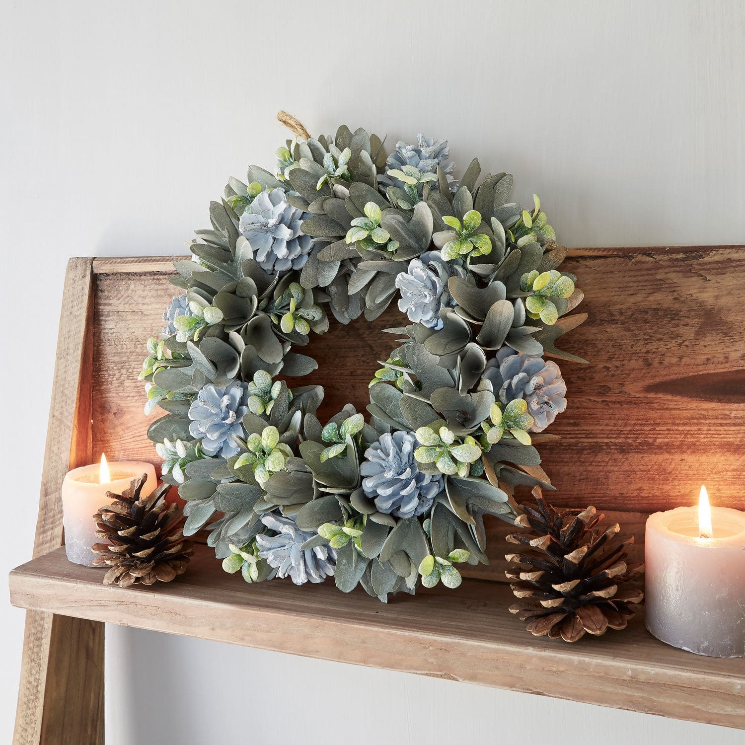 Krans Deinze Decoratieve krans van grijze bladeren en blauwe dennenappels op houten plank met kaarsen en dennenappels