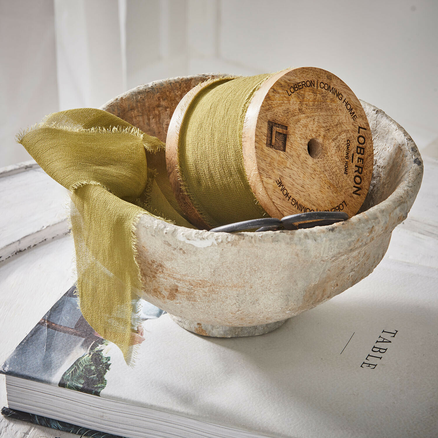 Natuurlijke stenen kom met groene stof en houten spoel op een boek over tafels