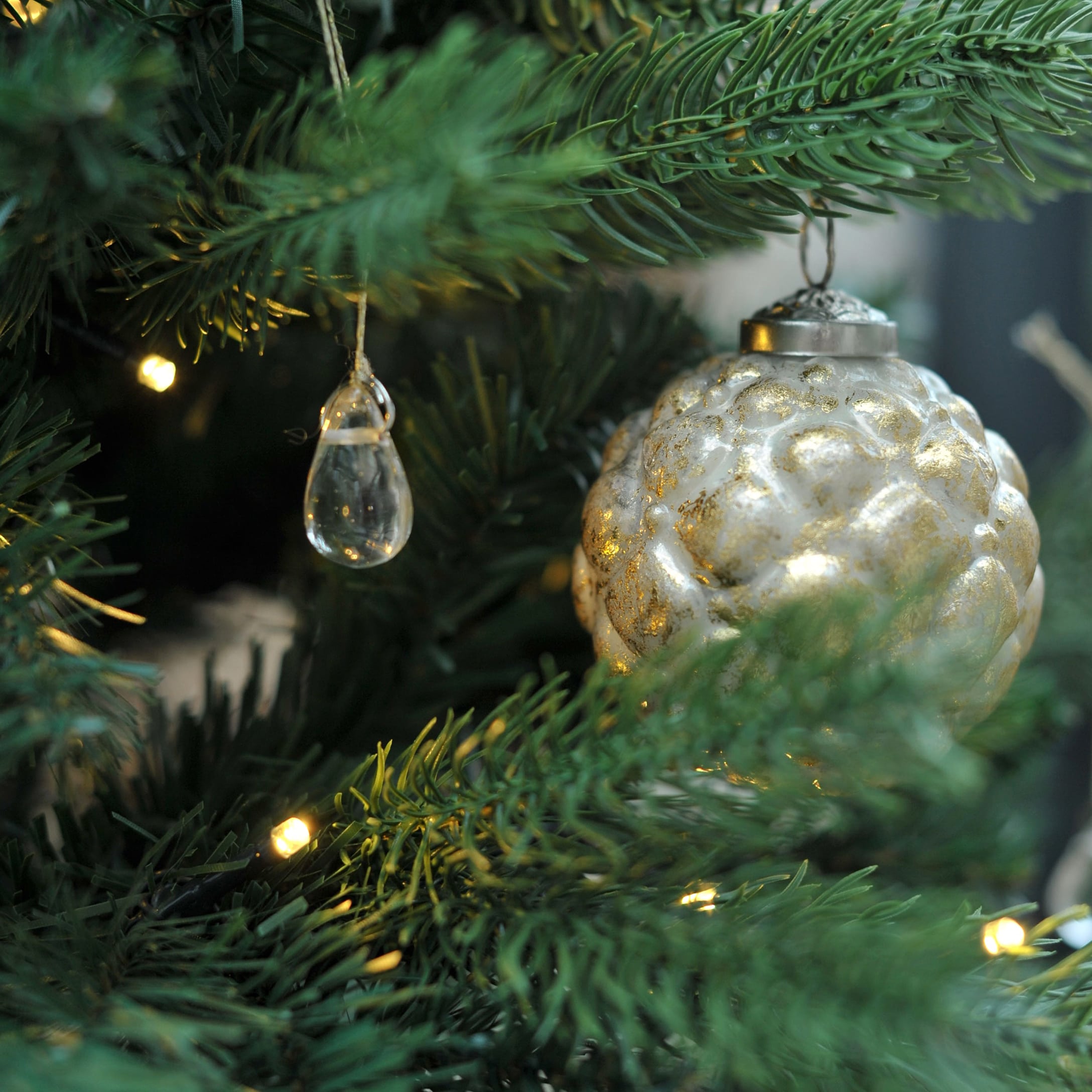 Gouden glazen kerstbal en doorzichtige hanger aan groene kerstboom met kerstverlichting